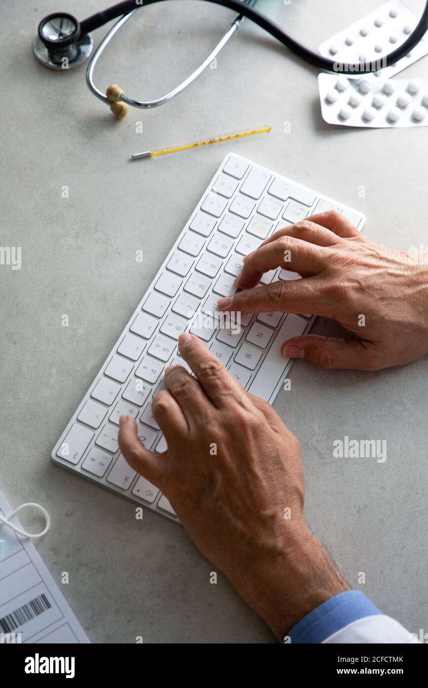 From above of senior male practitioner using wireless keyboard while conducting telemedicine consultation during quarantine Stock Photo