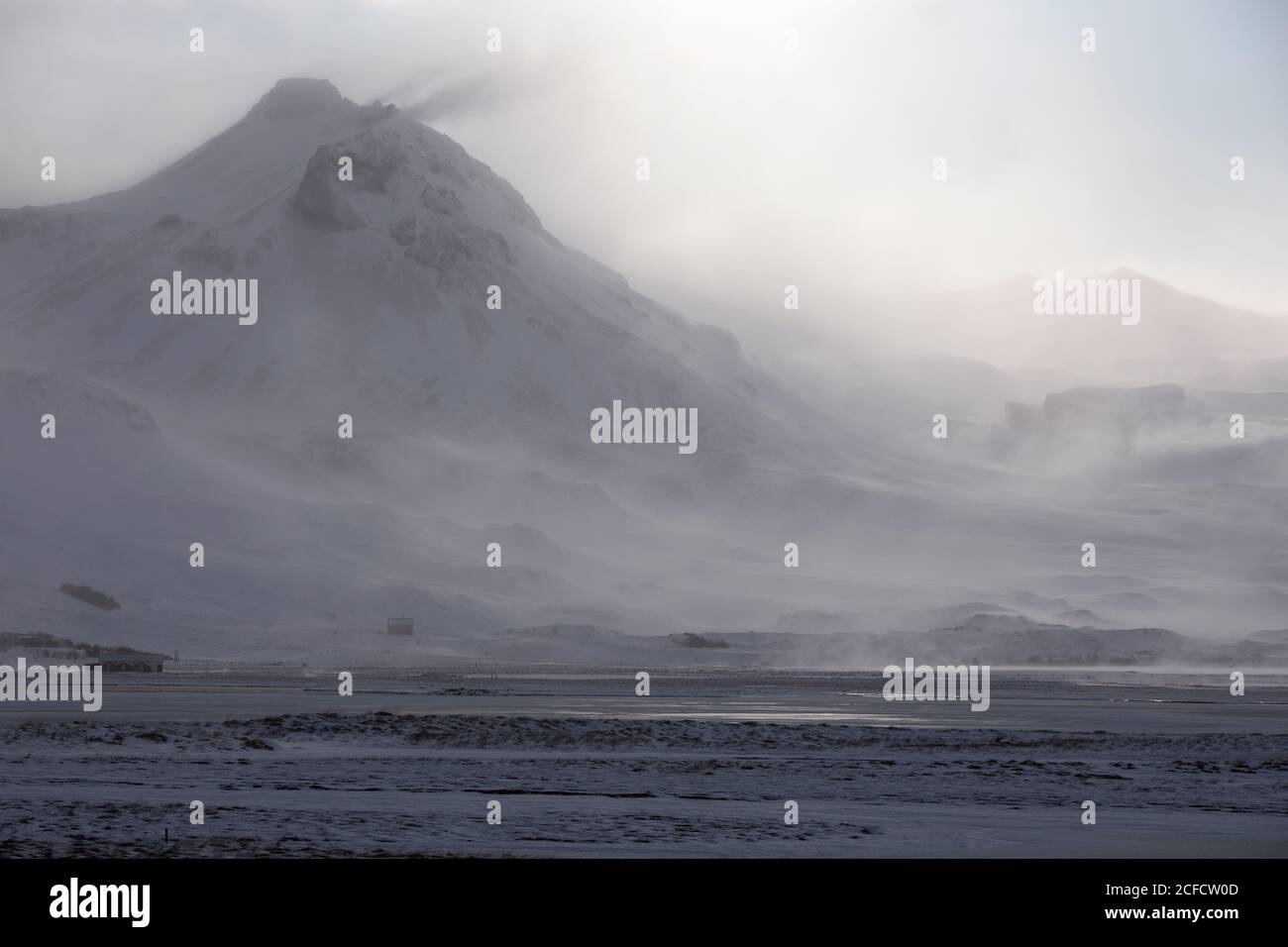 Severe wild landscape of snow capped volcano and mountain range during blizzard in winter day in Iceland Stock Photo
