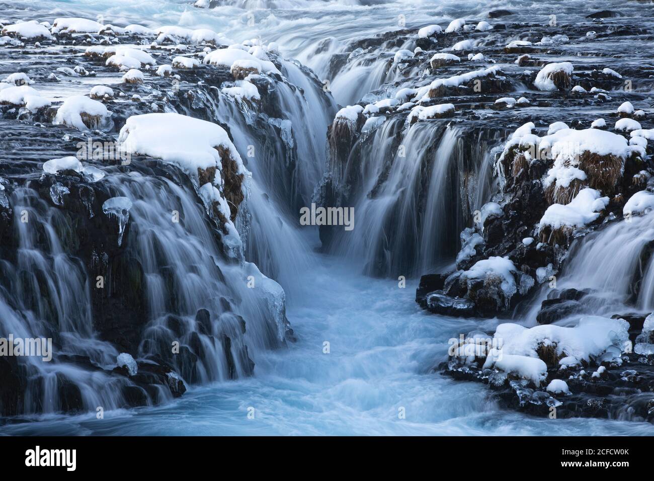 Amazing Nordic scenery of frozen waterfalls and river flowing through rough volcanic terrain covered with snow in Iceland Stock Photo