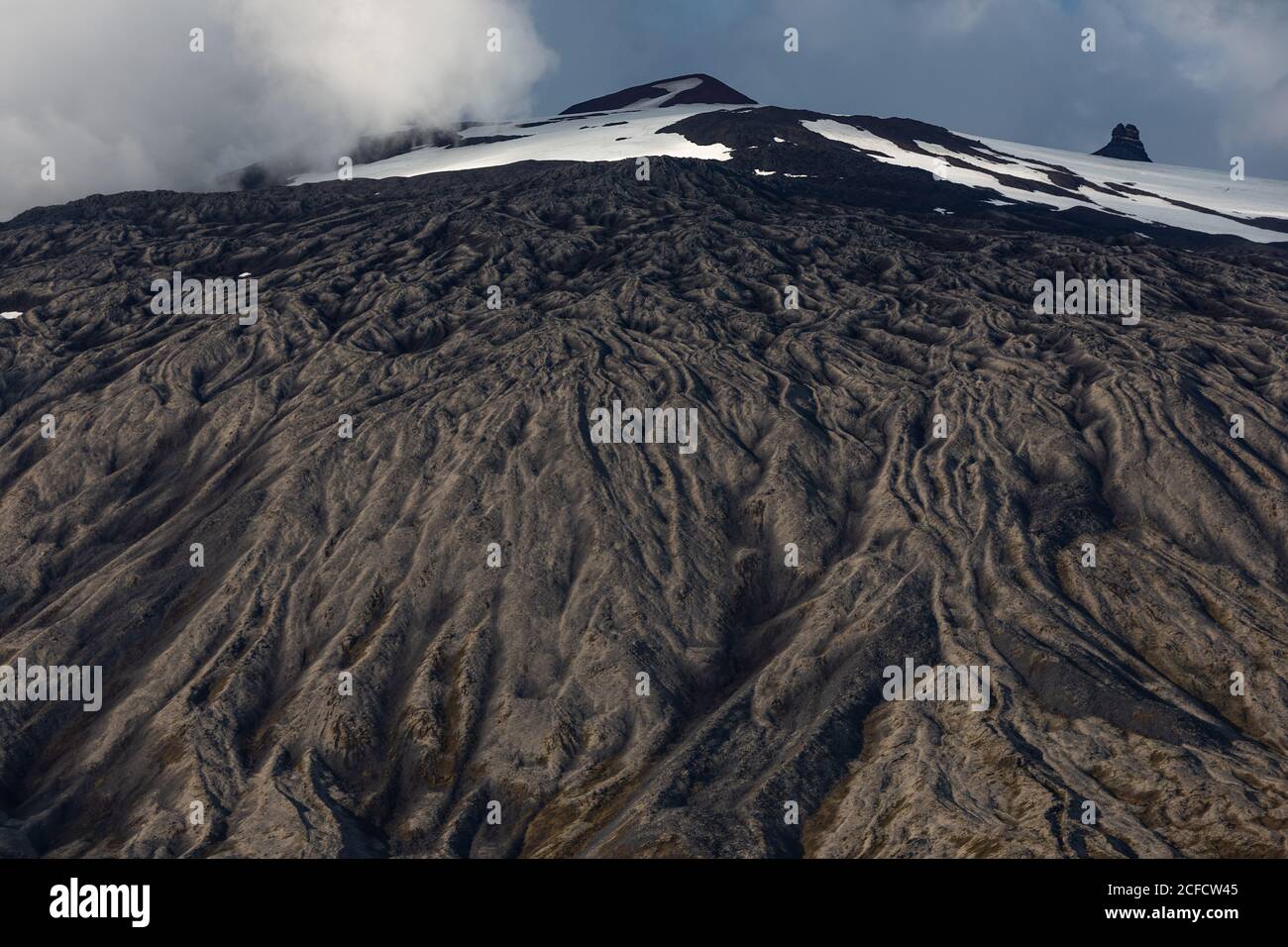 From below rough slope and snowy mountain peak against cloudy sky in Iceland Stock Photo