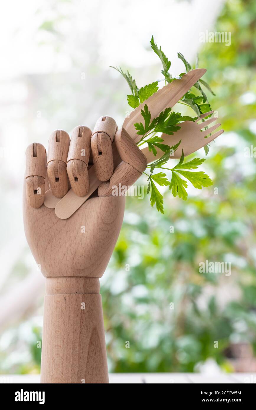 Creative mannequin hand with disposable fork and knife garnished with sprig of green parsley placed on table in garden Stock Photo