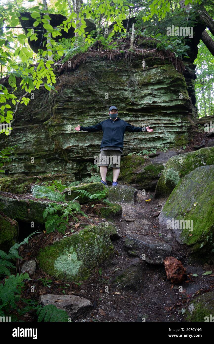 A woman wearing a mask with arms out at Panama Rocks Scenic Park, Chautauqua County, New York, USA, an ancient petrified forest of quartz conglomerate Stock Photo