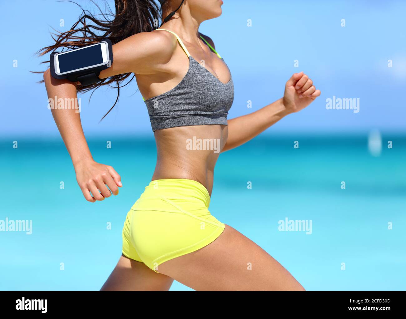 Fitness athlete woman running fast with speed wearing phone armband with touchscreen. Midsection crop showing muscular legs and thighs training glutes Stock Photo