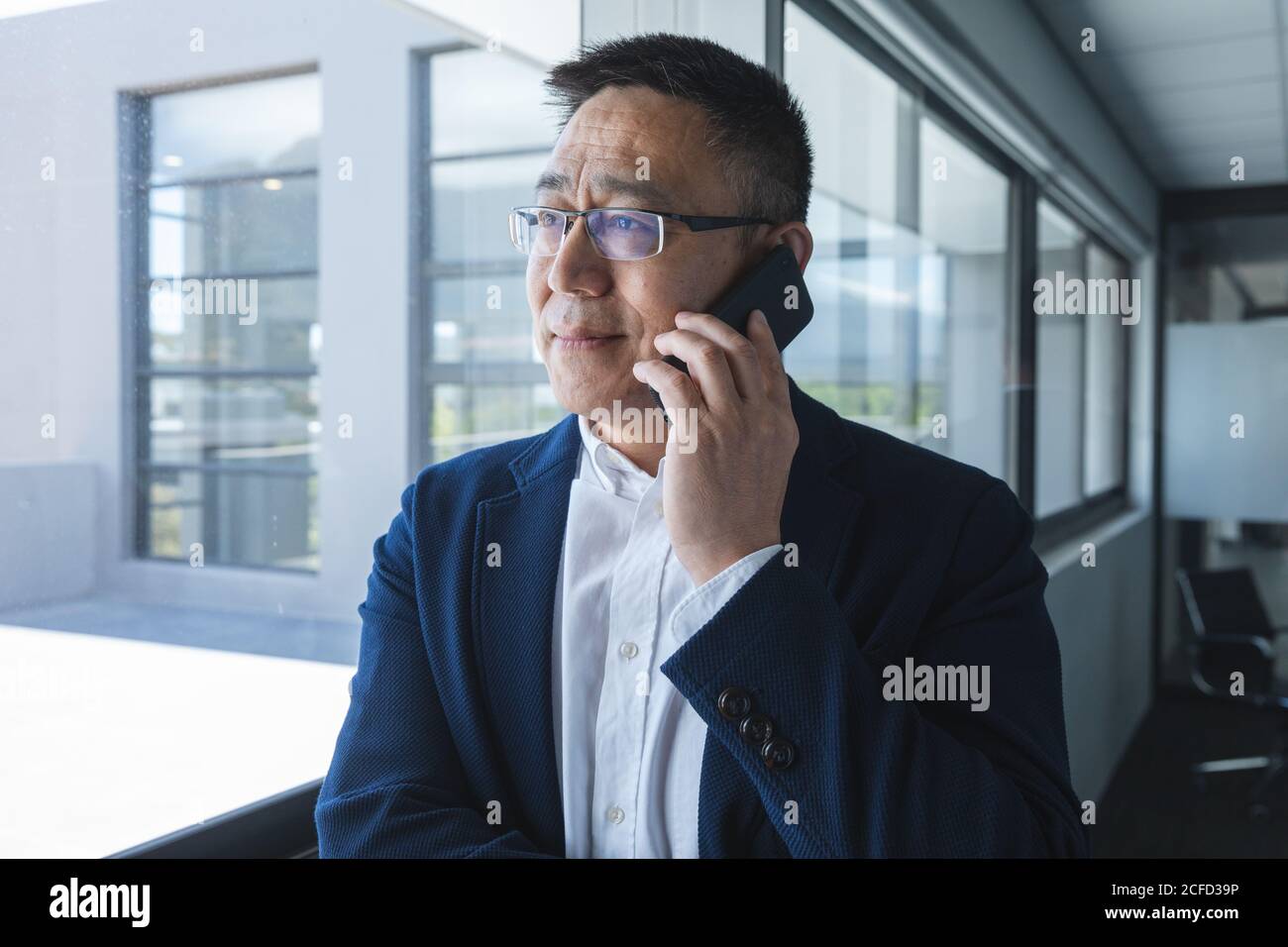 Senior businessman talking on his smartphone near window at modern office Stock Photo