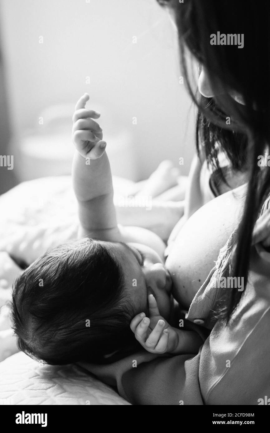 From above young mother holding on hands and breastfeeding newborn baby wrapped in blanket on bed at home Stock Photo