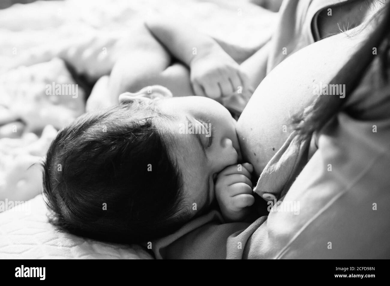 From above young mother holding on hands and breastfeeding newborn baby wrapped in blanket on bed at home Stock Photo