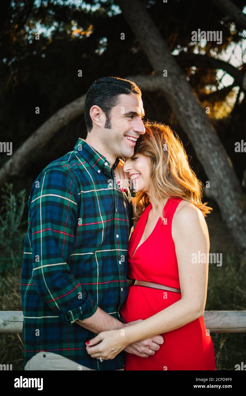 Handsome adult male smiling and hugging beautiful pregnant female from ...