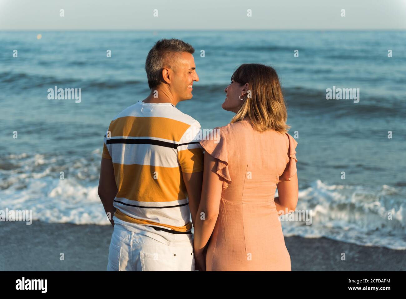 Adult man hugging Woman from behind standing on beach near waving sea ...