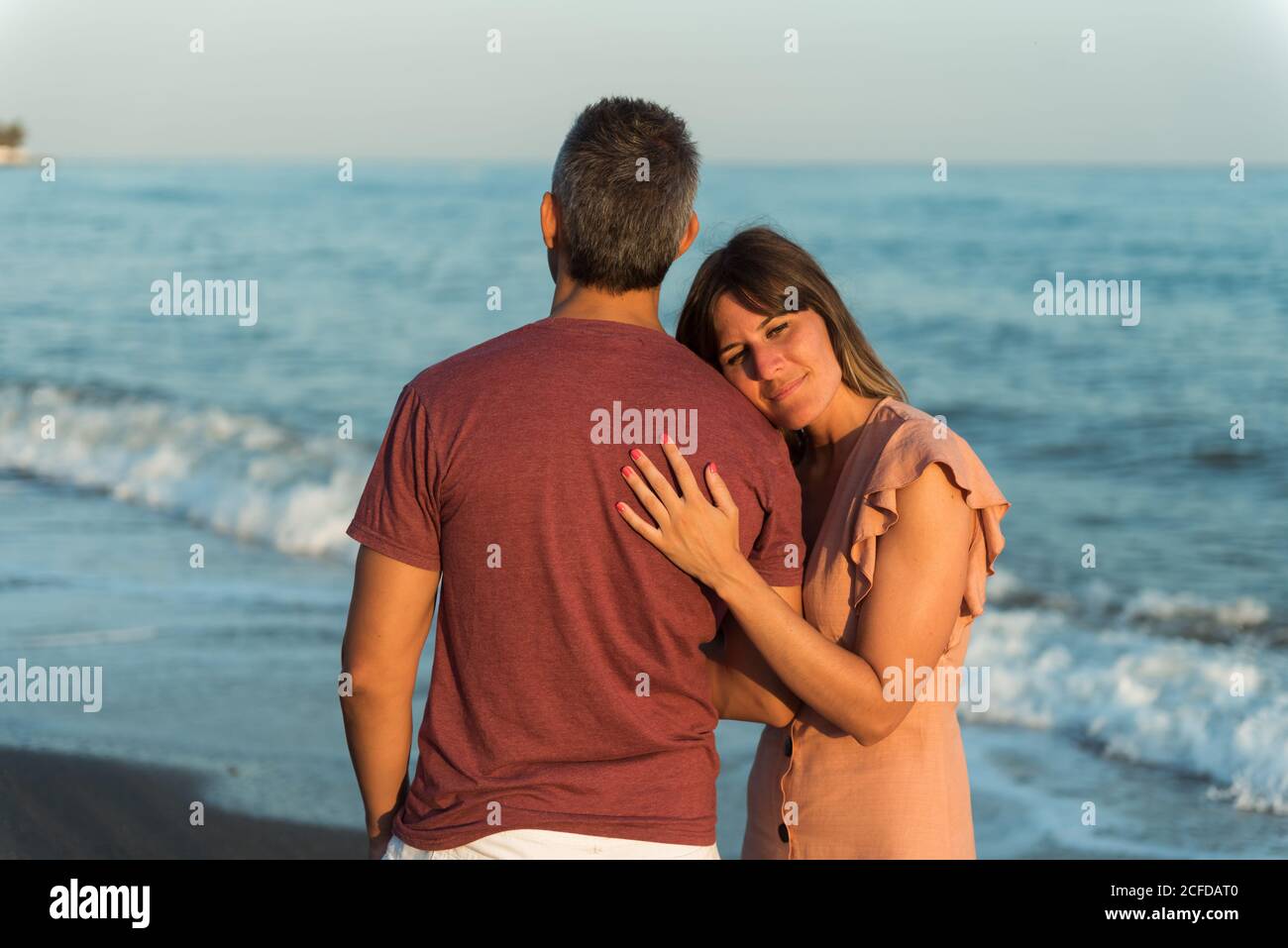 Adult man hugging Woman from behind standing on beach near waving sea ...