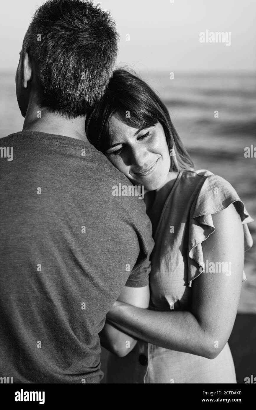 Adult man hugging Woman from behind standing on beach near waving sea ...
