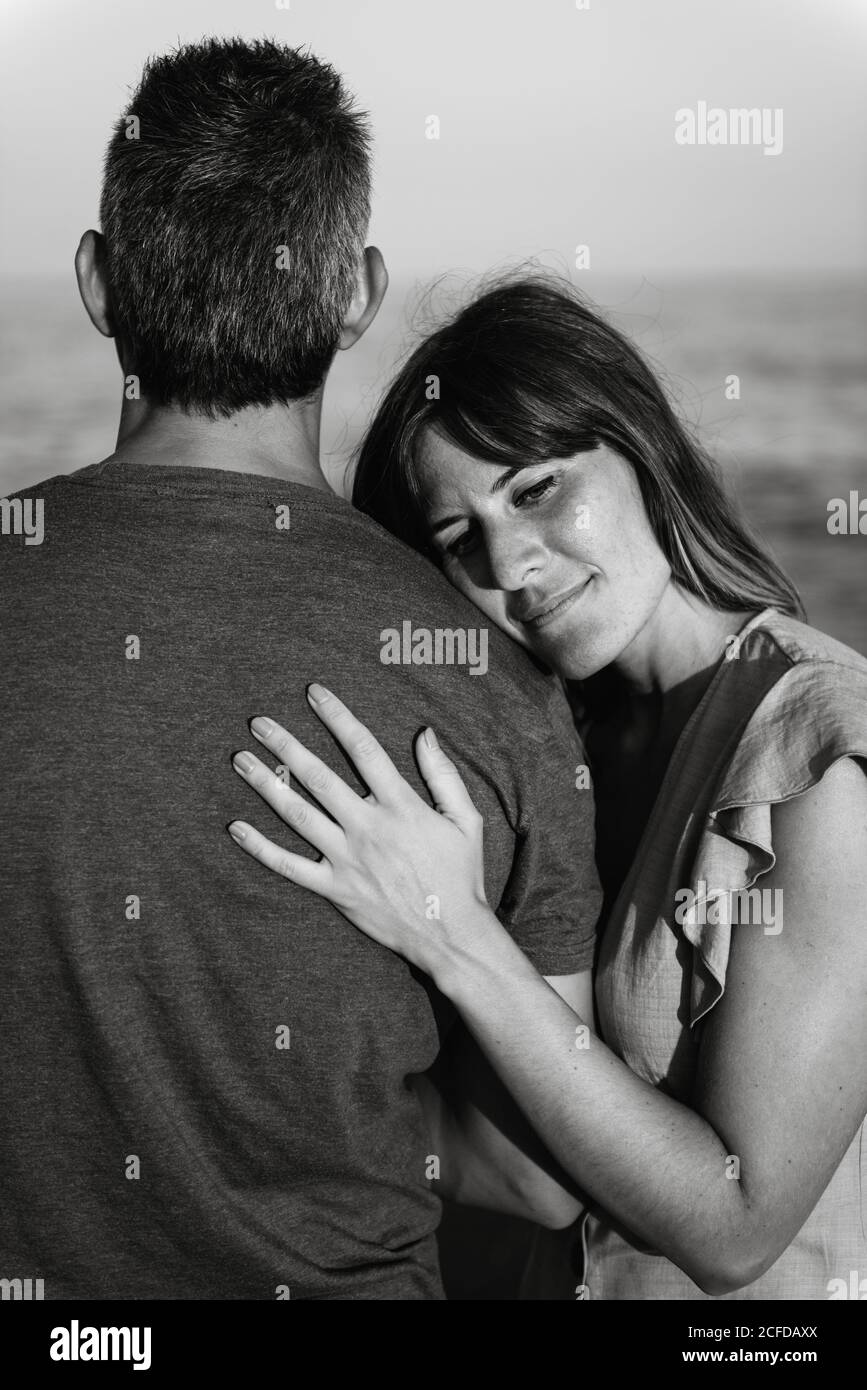 Adult man hugging Woman from behind standing on beach near waving sea ...