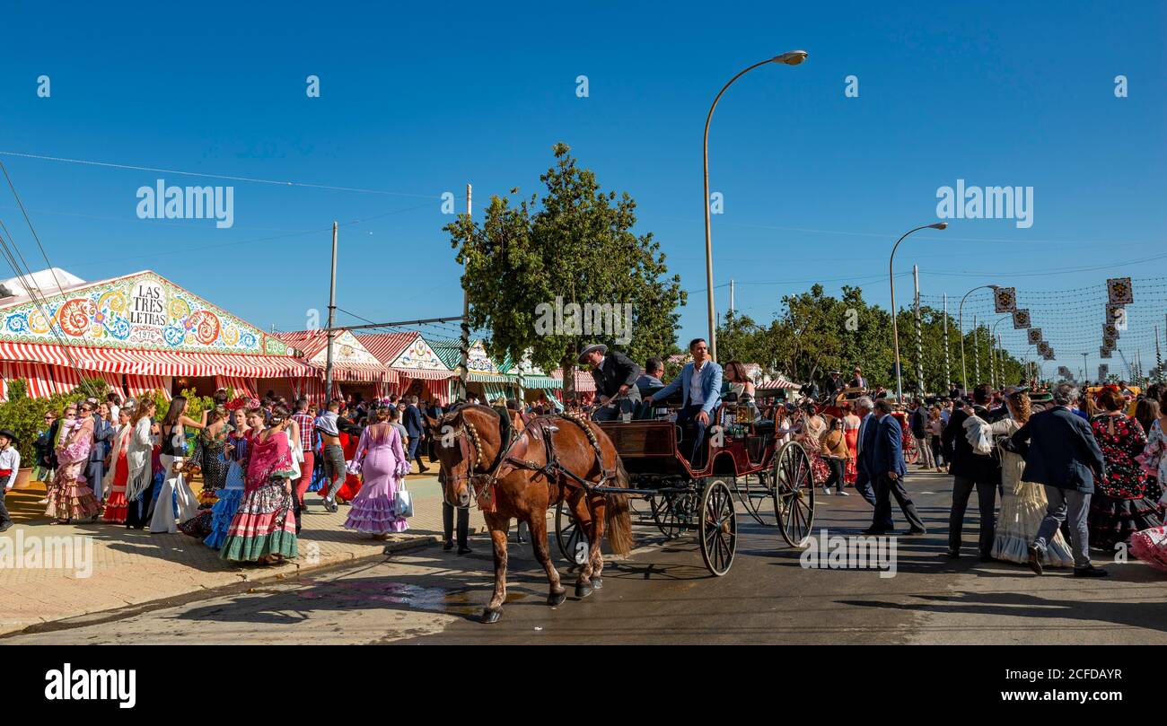 Street with casetas, traditionally dressed visitors and horse-drawn carriage, Feria de Abril, Seville, Andalusia, Spain Stock Photo