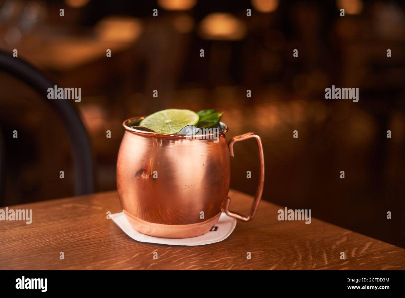 Classic alcohol cocktail Moscow Mule based on vodka with ginger beer and lime juice served in copper mug decorated with lemon slice on wooden table Stock Photo