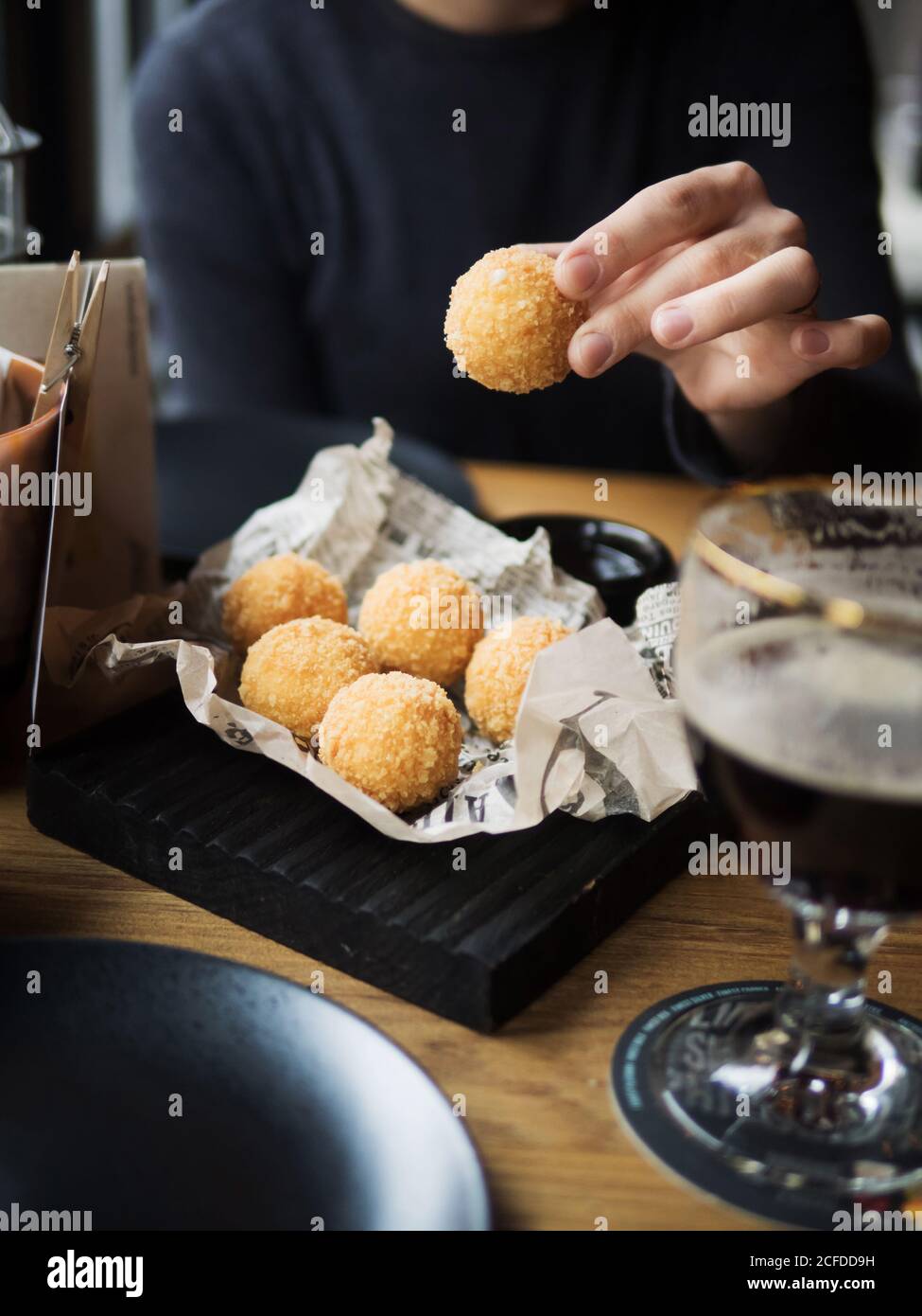 Crop female holding delicious cheese ball with mozzarella filling while sitting at table in cafe Stock Photo