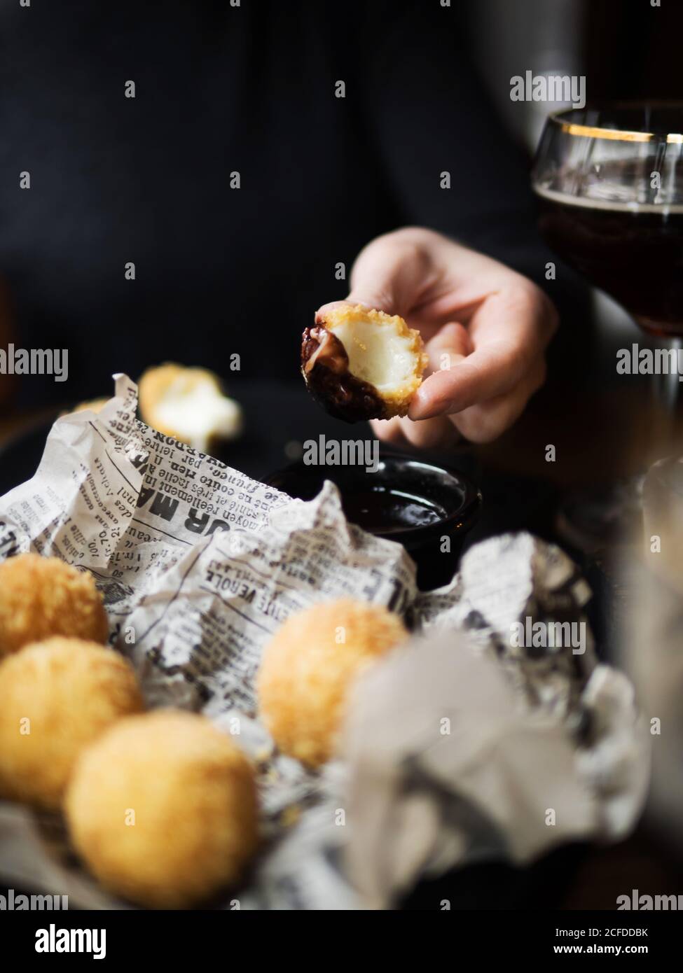 Crop unrecognizable female holding delicious cheese ball with mozzarella filling while sitting at table in cafe Stock Photo