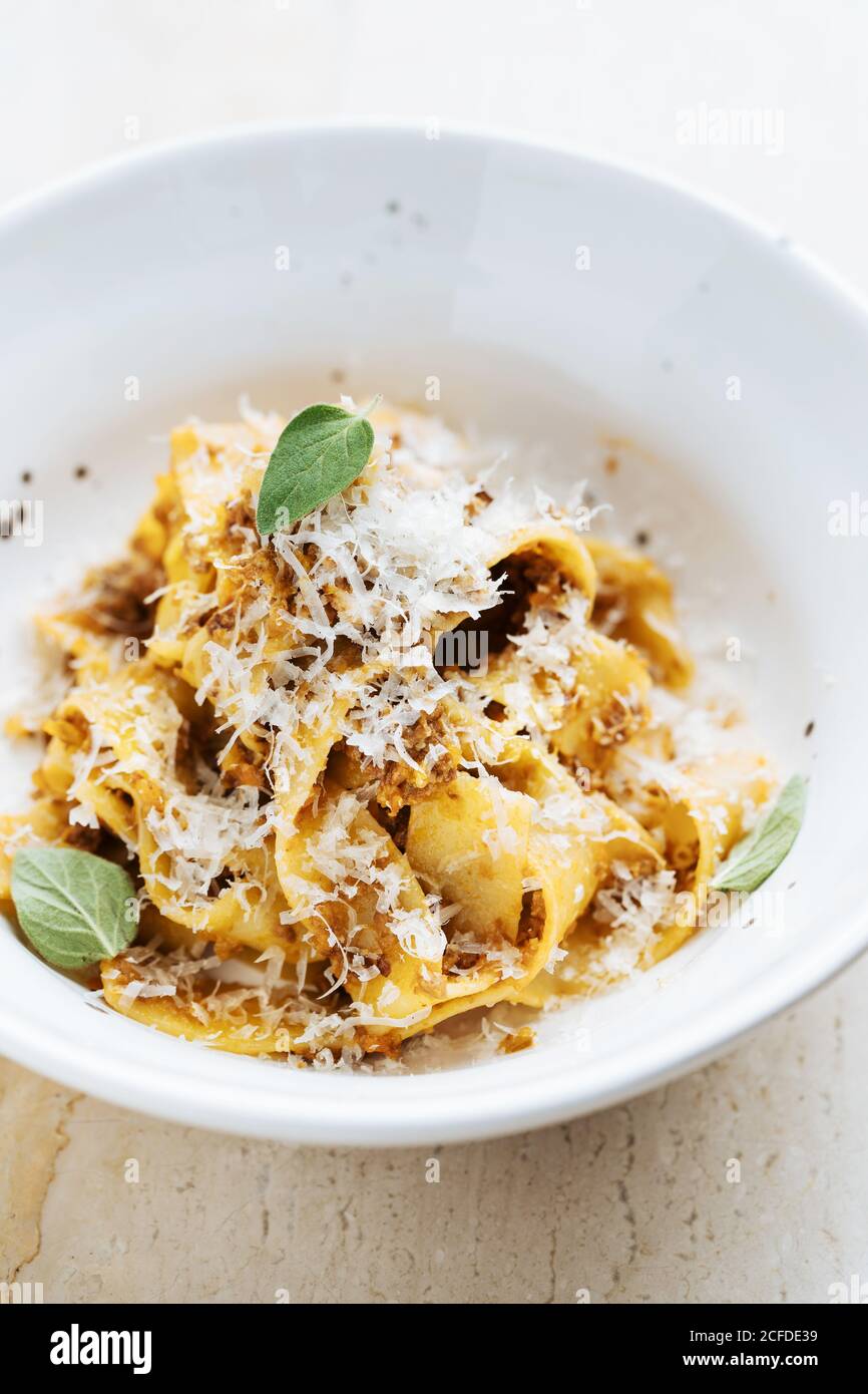 From above of tasty dish with wide pasta sprinkled with cheese and decorated with fresh mint in restaurant Stock Photo