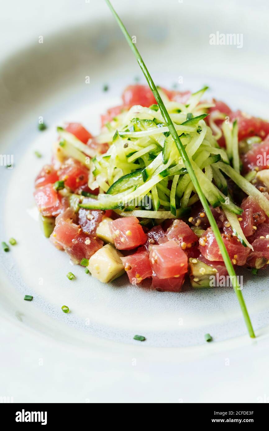 Top view of square pieces of red tuna served with slices of cucumber and herbs on white plate in restaurant Stock Photo