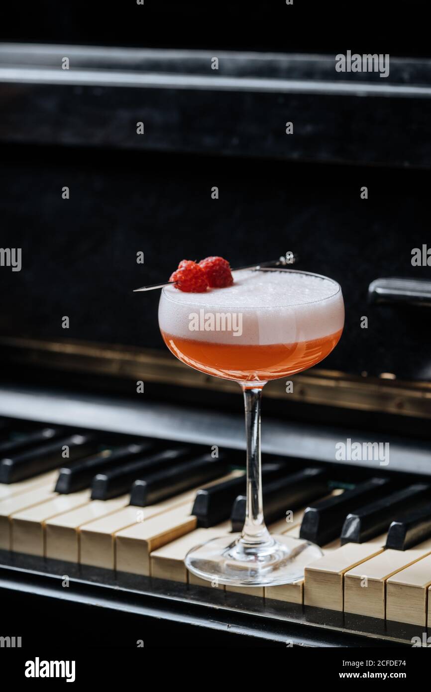 https://c8.alamy.com/comp/2CFDE74/red-alcohol-cocktail-in-stylish-glass-with-white-foam-decorated-with-fresh-raspberry-on-piano-keys-in-restaurant-2CFDE74.jpg