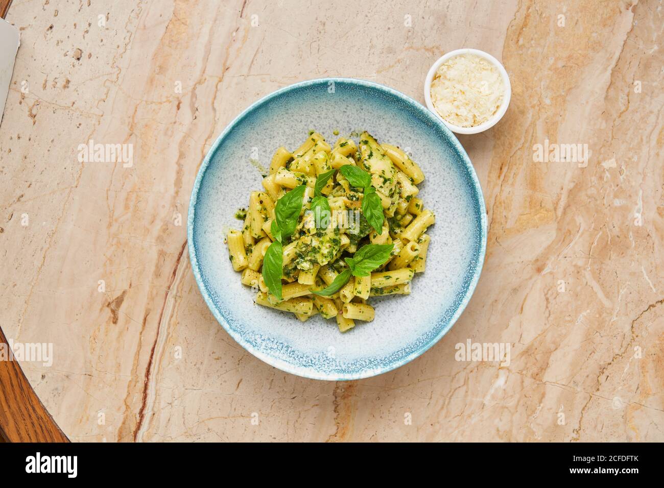 Top view of boiled noodles decorated with green herbs on blue plate served with small bowl of grated cheese Stock Photo