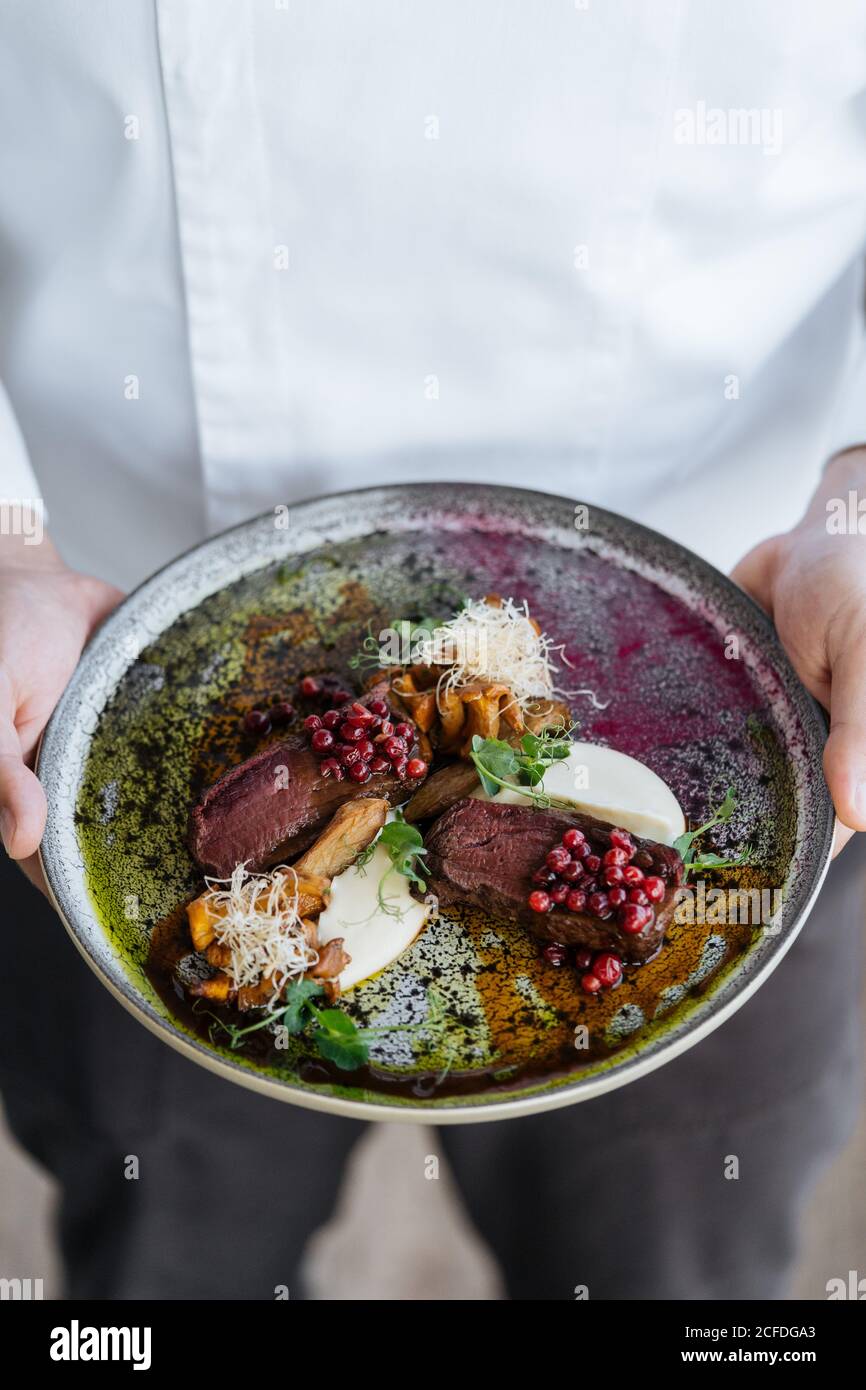 From above unrecognizable person holding plate delicious rare steak with sweet cranberry sauce served with herbs and mushrooms with cheese Stock Photo