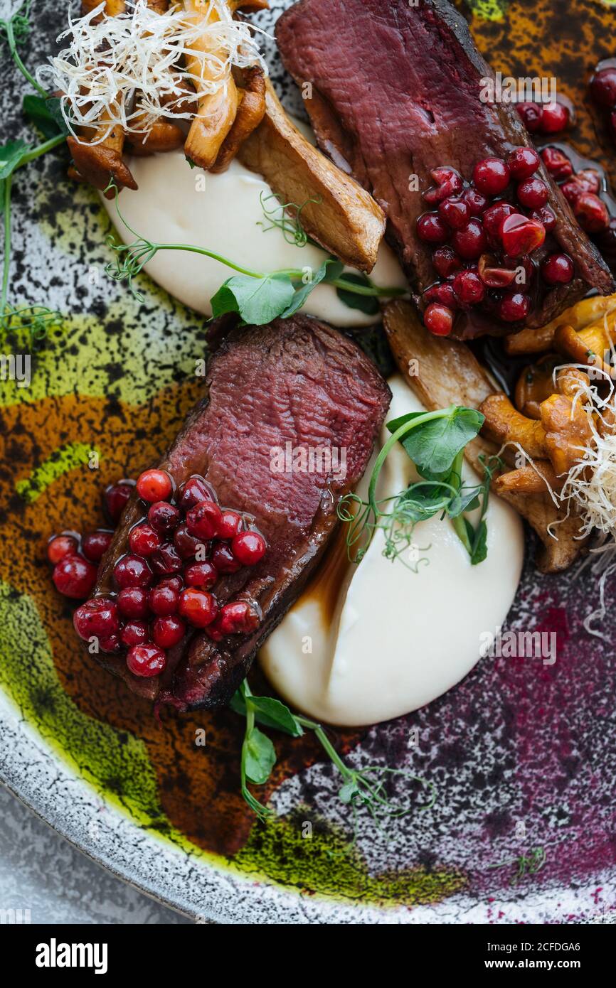 From above delicious rare steak with sweet cranberry sauce served with herbs and mushrooms with cheese on plate Stock Photo