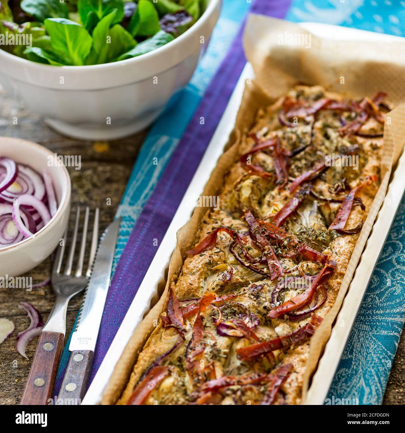 Foccacia fresh from the oven, in a rectangular tart pan, with green salad, extra red onions and artichokes Stock Photo