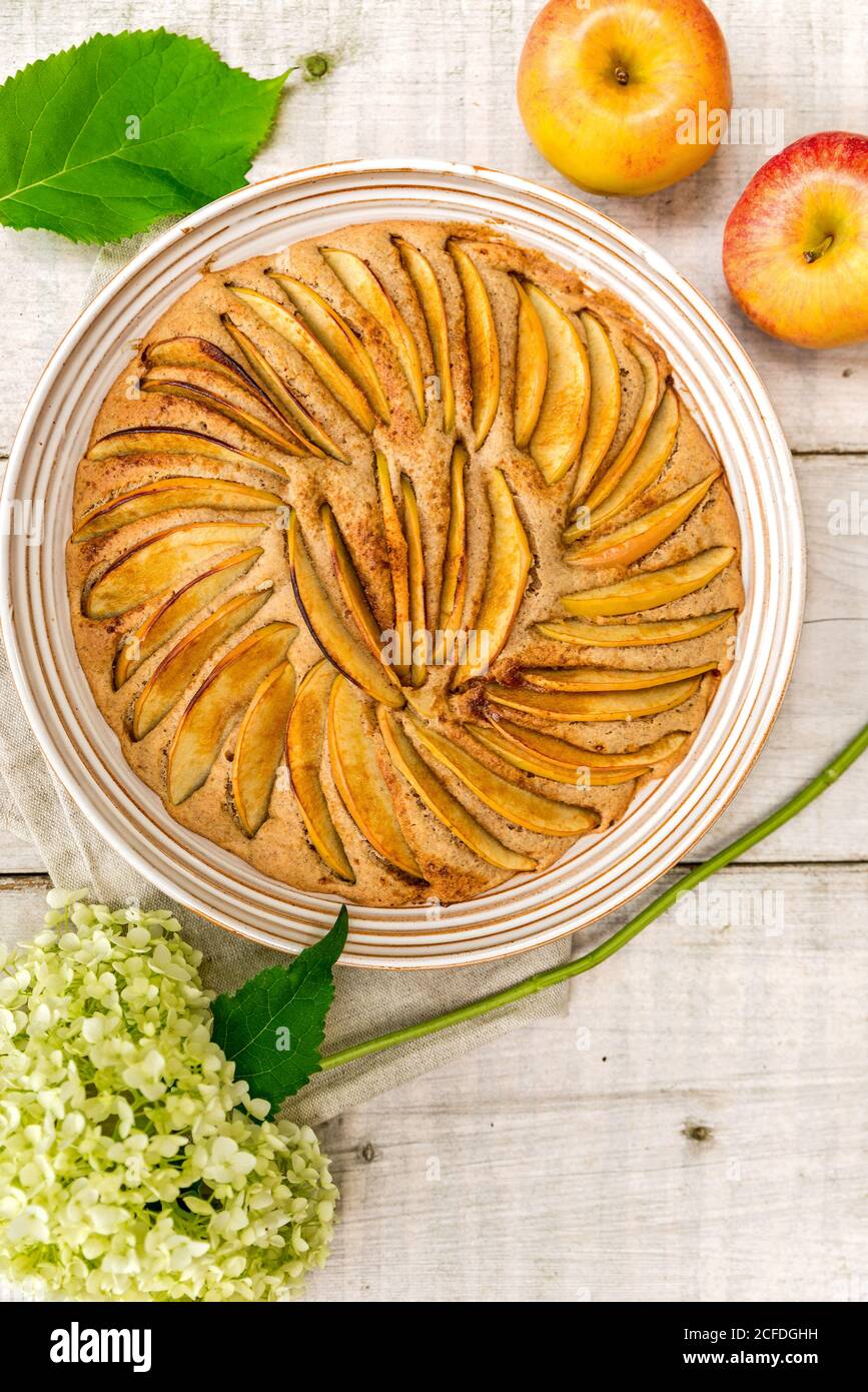 Apple pie baked in a round shape and decorated with apple slices, decorated with two apples and a white hydrangea flower Stock Photo