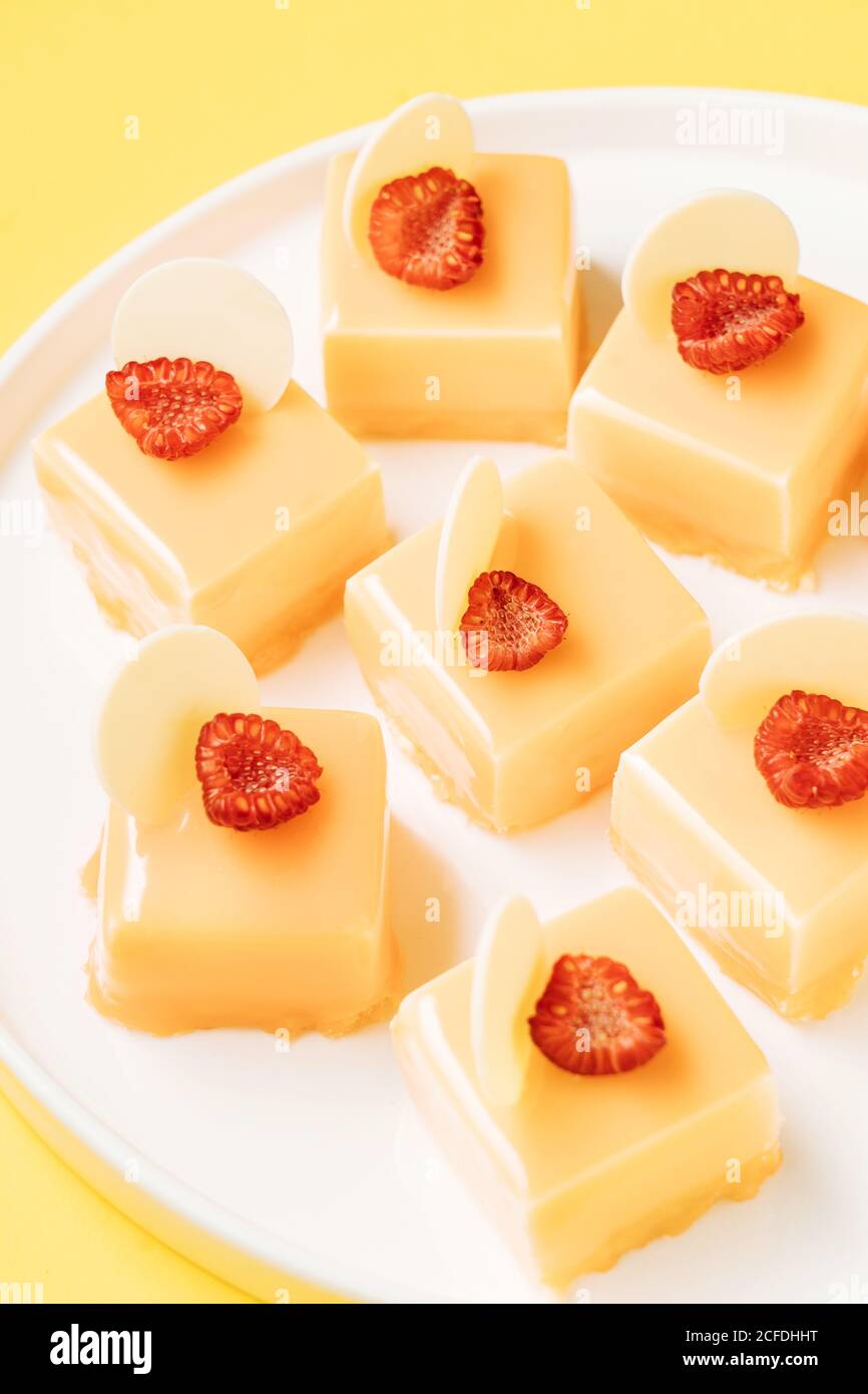 Closeup pieces of scrumptious pastry decorated with halves of fresh raspberries and white chocolate and placed on plate on yellow background Stock Photo