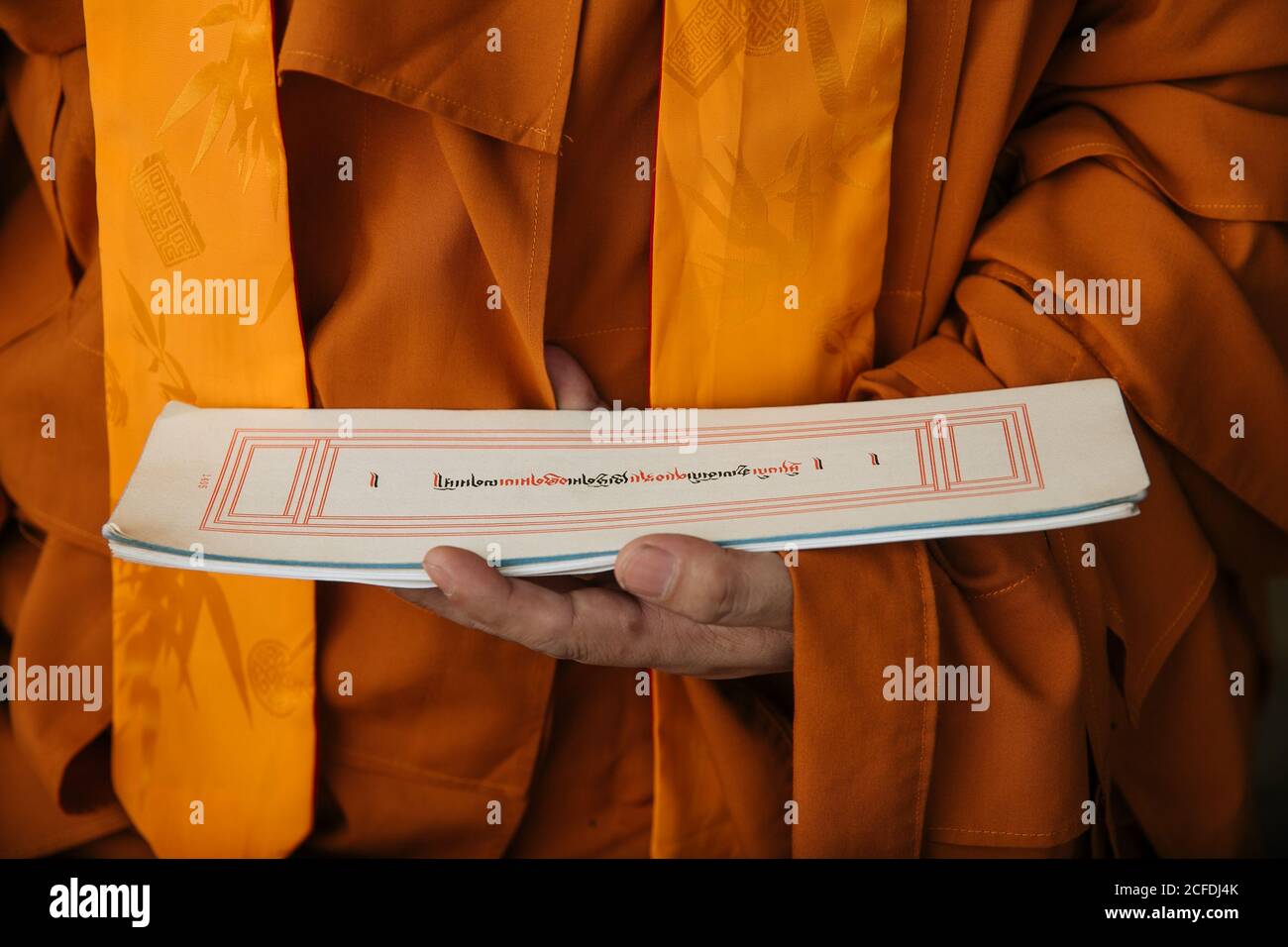 Crop Tibetan Buddhist monk in orange clothes holding paper with holy ritual text Stock Photo