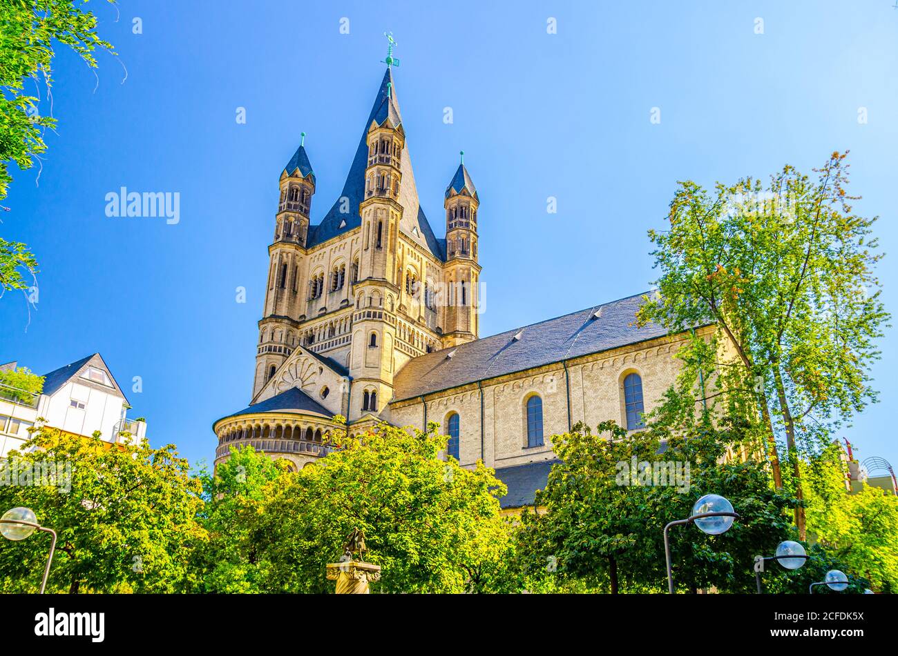 The Great Saint Martin Roman Catholic Church Romanesque architecture style building with spire on tower and green trees crown foreground, blue clear sky in summer day, North Rhine-Westphalia, Germany Stock Photo
