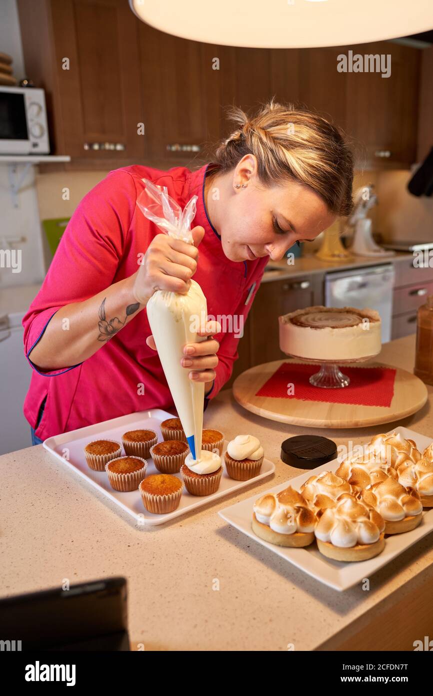 Woman chef in vibrant uniform using piping bag to filling tarts with whipped  egg whites cream while cooking homemade delicious cookies with meringue in  light modern kitchen Stock Photo - Alamy
