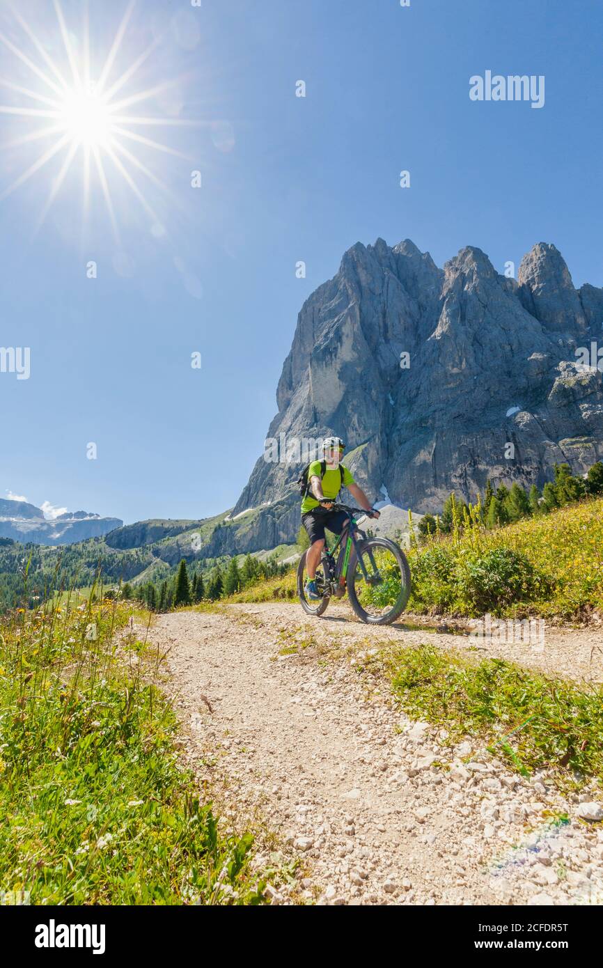 cyclist with an electric mountain bike (e-bike) pedaling at the foot of Sassolungo Langkofel, Val Gardena, Grödental, South Tyrol, Dolomites, Italy Stock Photo