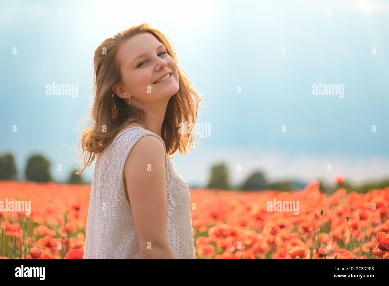Young beaming girl in the poppy field, smiling, looking at camera Stock Photo