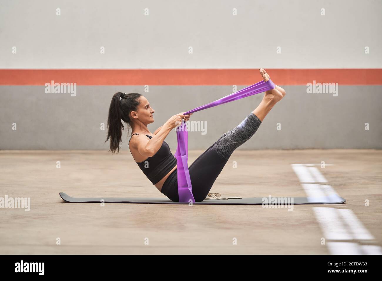 Cheerful athletic female in activewear sitting barefoot on mat and