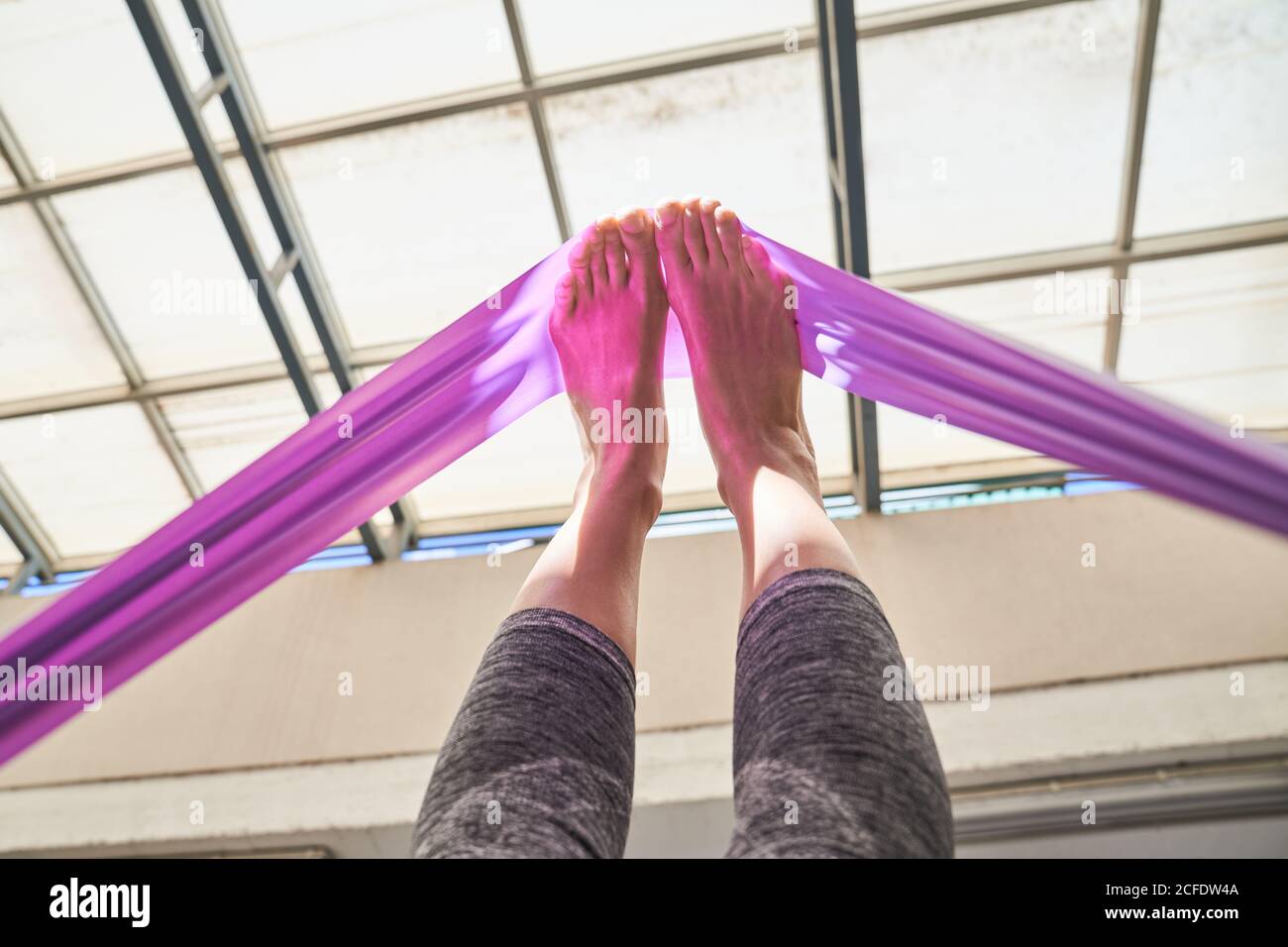 From below of barefoot female in sport leggings stretching muscles with resistance band during training in gym Stock Photo