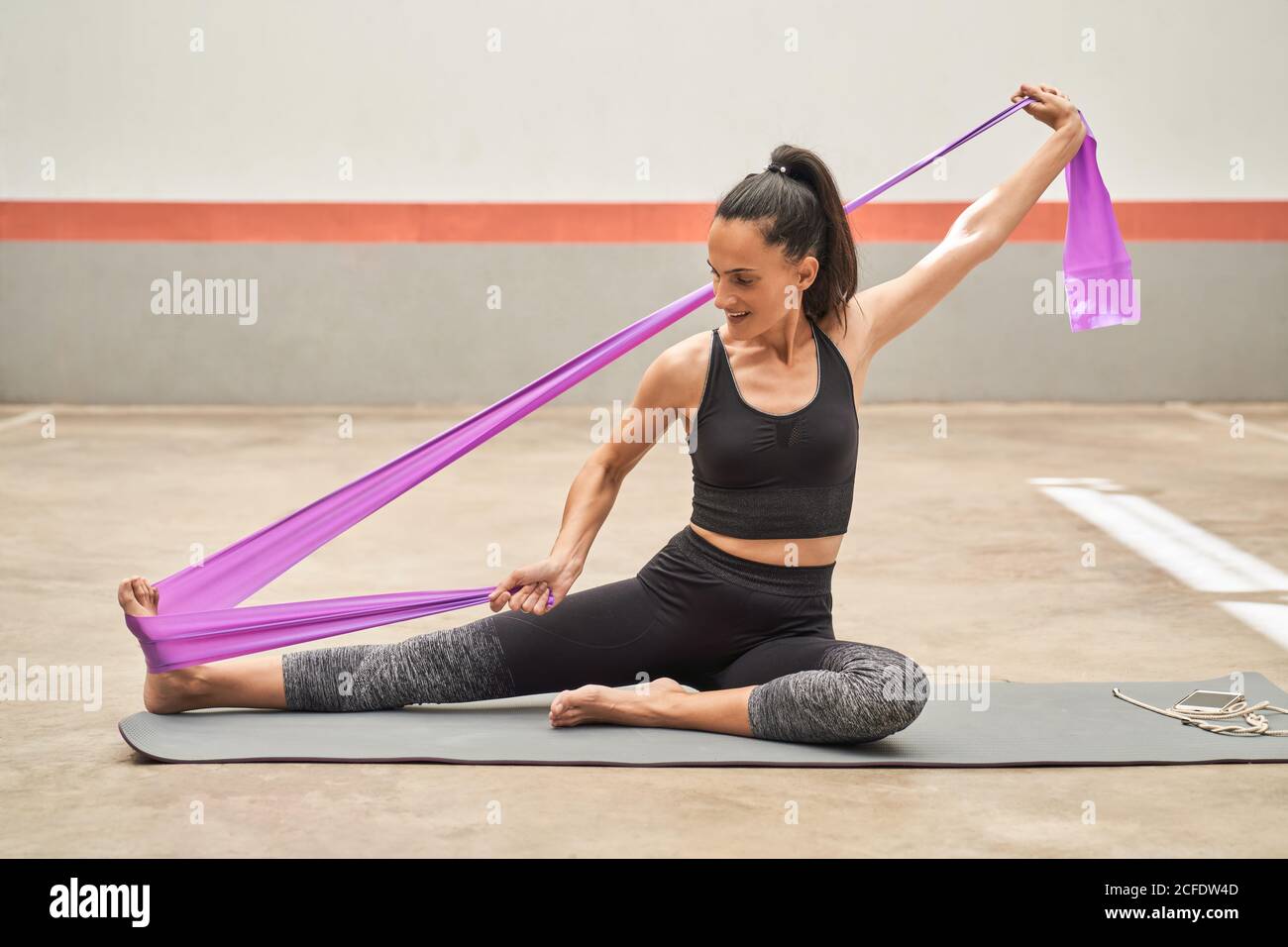 Cheerful athletic female in activewear sitting barefoot on mat and