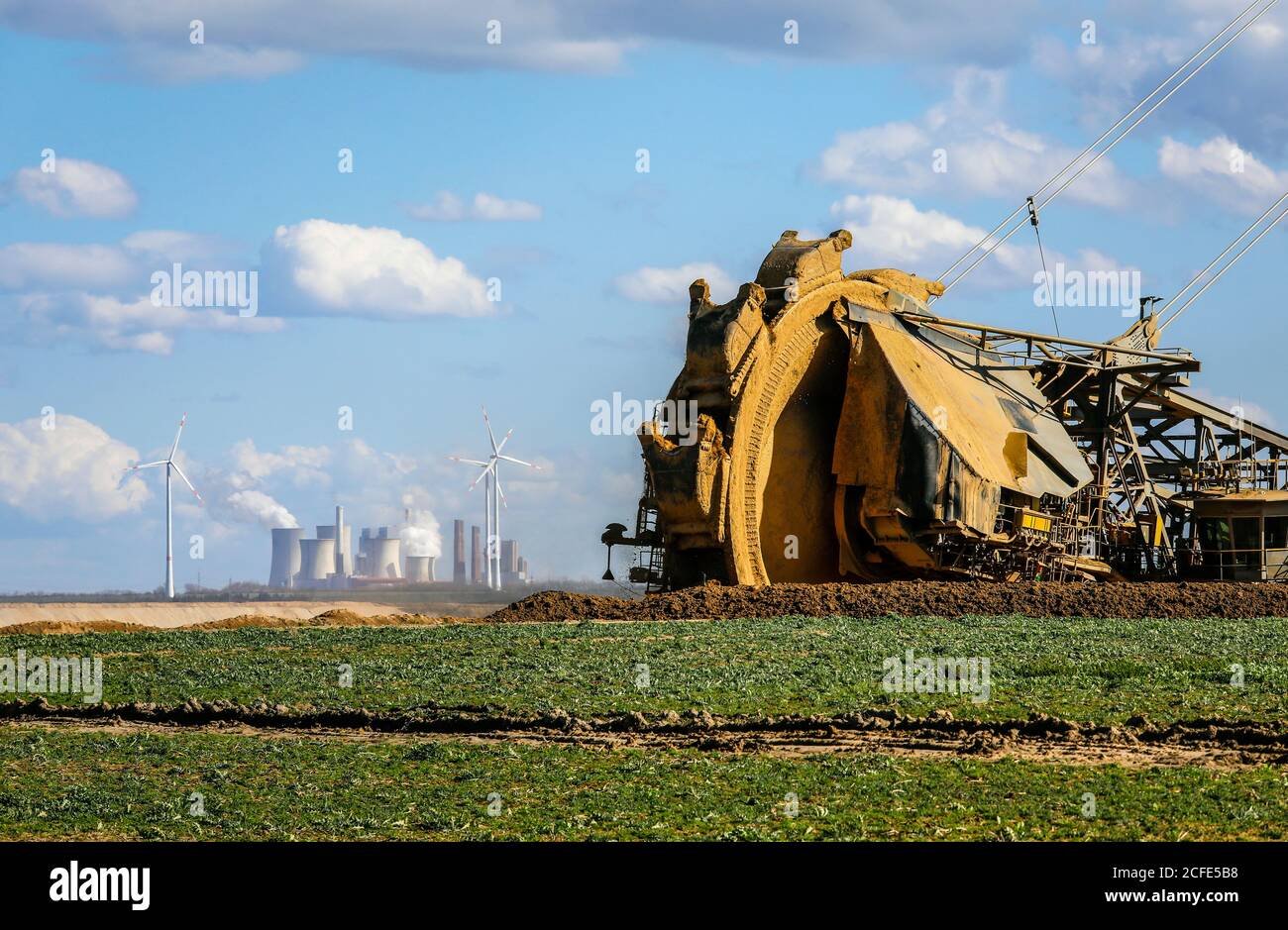 Bucket-wheel excavator in the RWE lignite mine Garzweiler dredges at the demolition edge near Keyenberg, a wind farm in the back and the Stock Photo