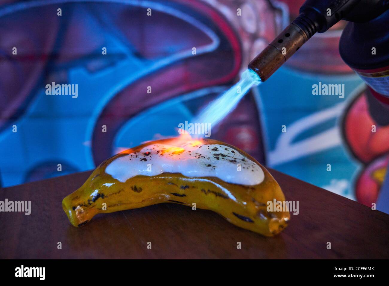 faceless chef using gas torch and grilling shiny white meringue on banana shaped pastry in restaurant Stock Photo