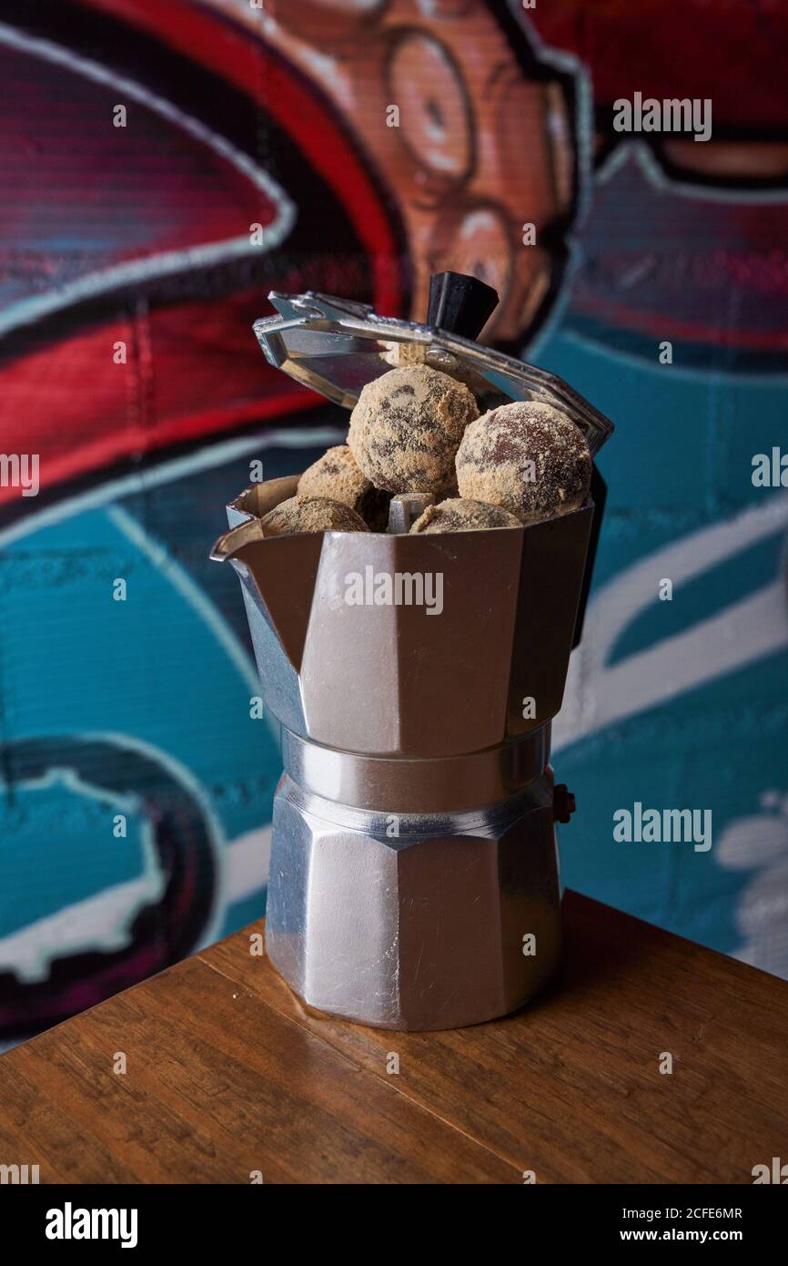 From above of stainless stove coffee maker with round balls of delicious chocolate truffles served on table against wall on graffiti Stock Photo
