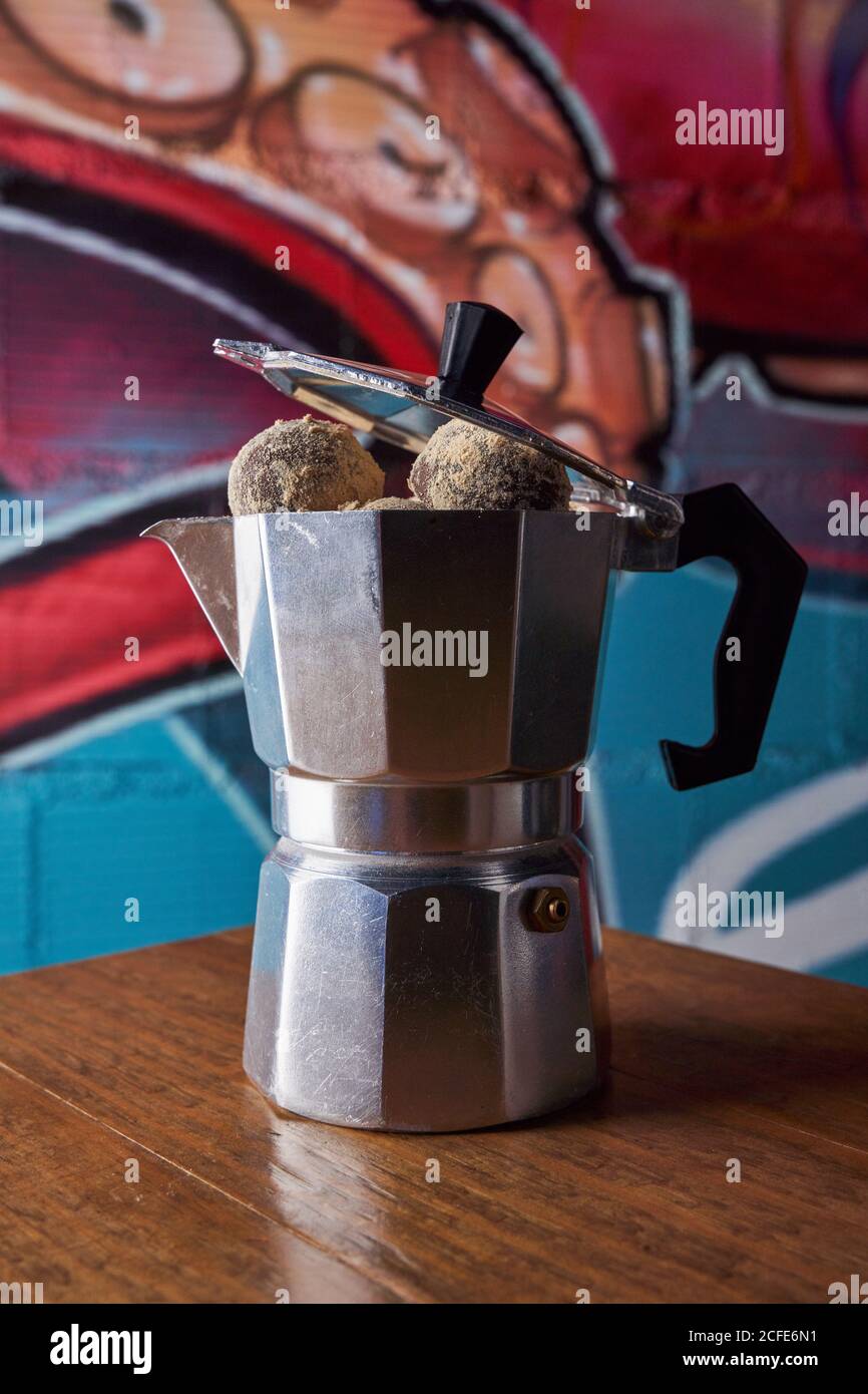 From above of stainless stove coffee maker with round balls of delicious chocolate truffles served on table against wall on graffiti Stock Photo