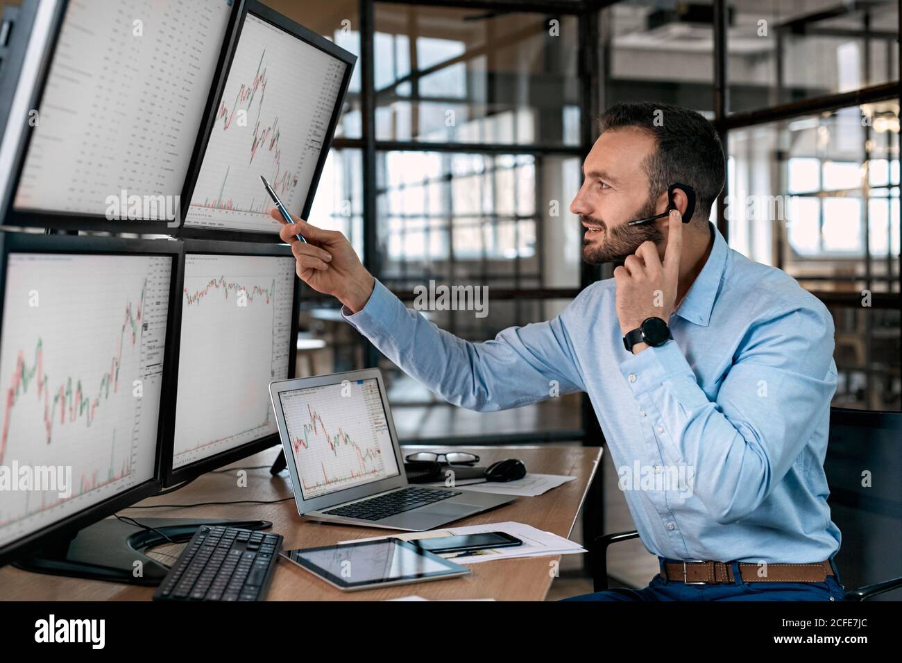 Stock Traiding. Trader wearing headset sitting at office in front of  monitors with data chart doing online trading training explaining supply  and Stock Photo - Alamy
