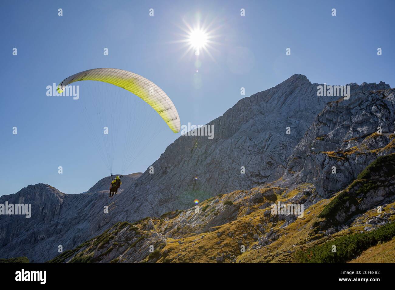 Paraglider at Osterfelder against Alpspitze (Wetterstein Mountains), blue sky, sun, back light, Garmisch-Partenkirchen, Upper Bavaria, Bavaria, Stock Photo