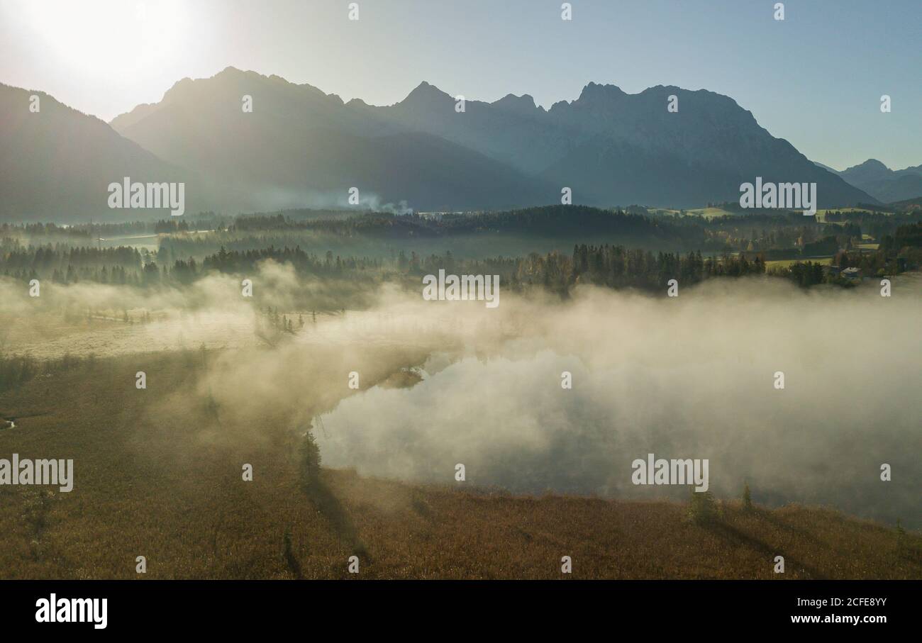 Aerial view mist at the Barmsee against the Karwendel mountains, blue sky, trees, lake shore, sun, back light, Krün, Garmisch-Partenkirchen, Upper Stock Photo