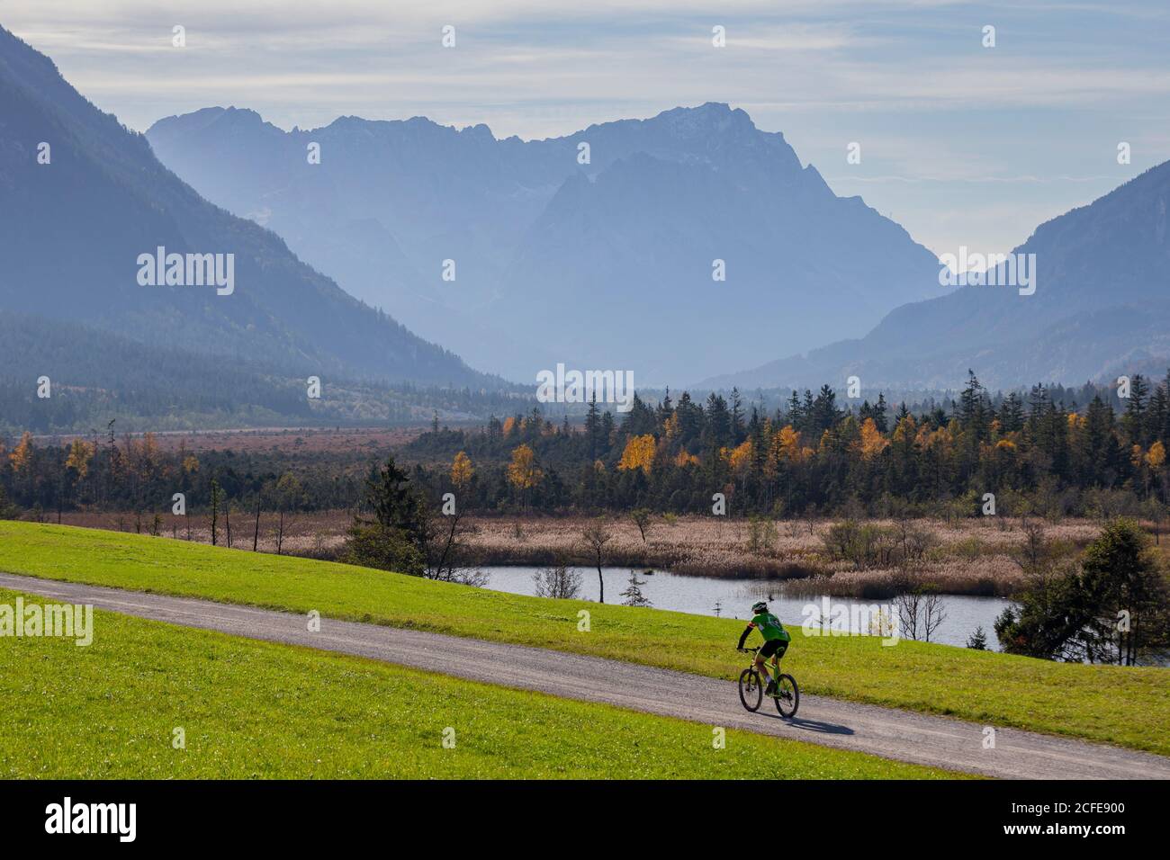 Mountain bike riders at the Seven Springs in Eschenlohe in autumn against Wetterstein Mountains with Alpspitze, Waxensteins and Zugspitze, blue sky, Stock Photo