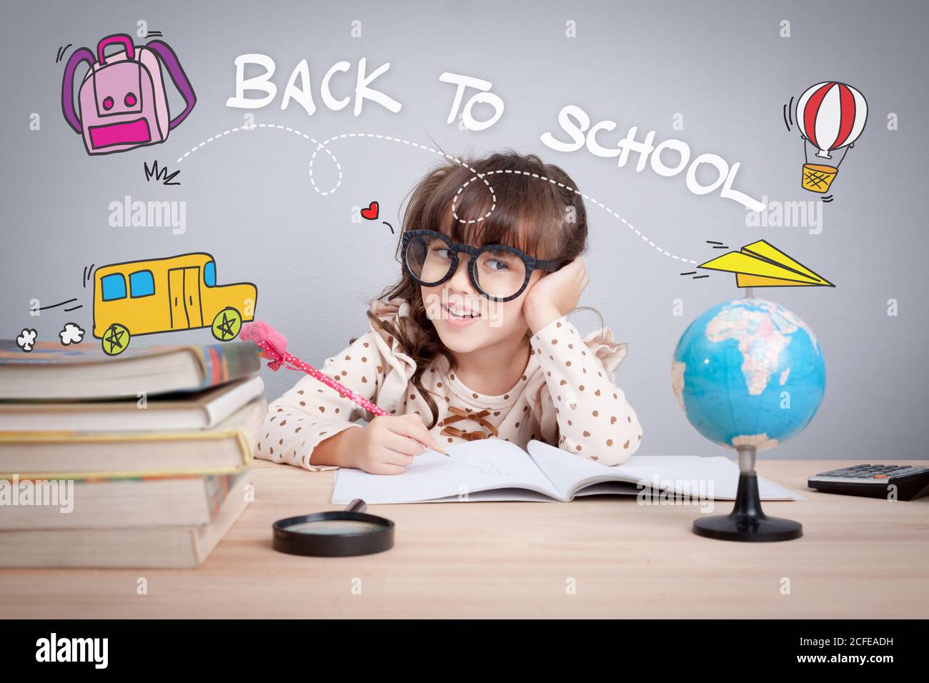 back to school  concept. cute little girl wear glasses do homework at home with word back to school and cute cartoon on head. learning, teaching and e Stock Photo