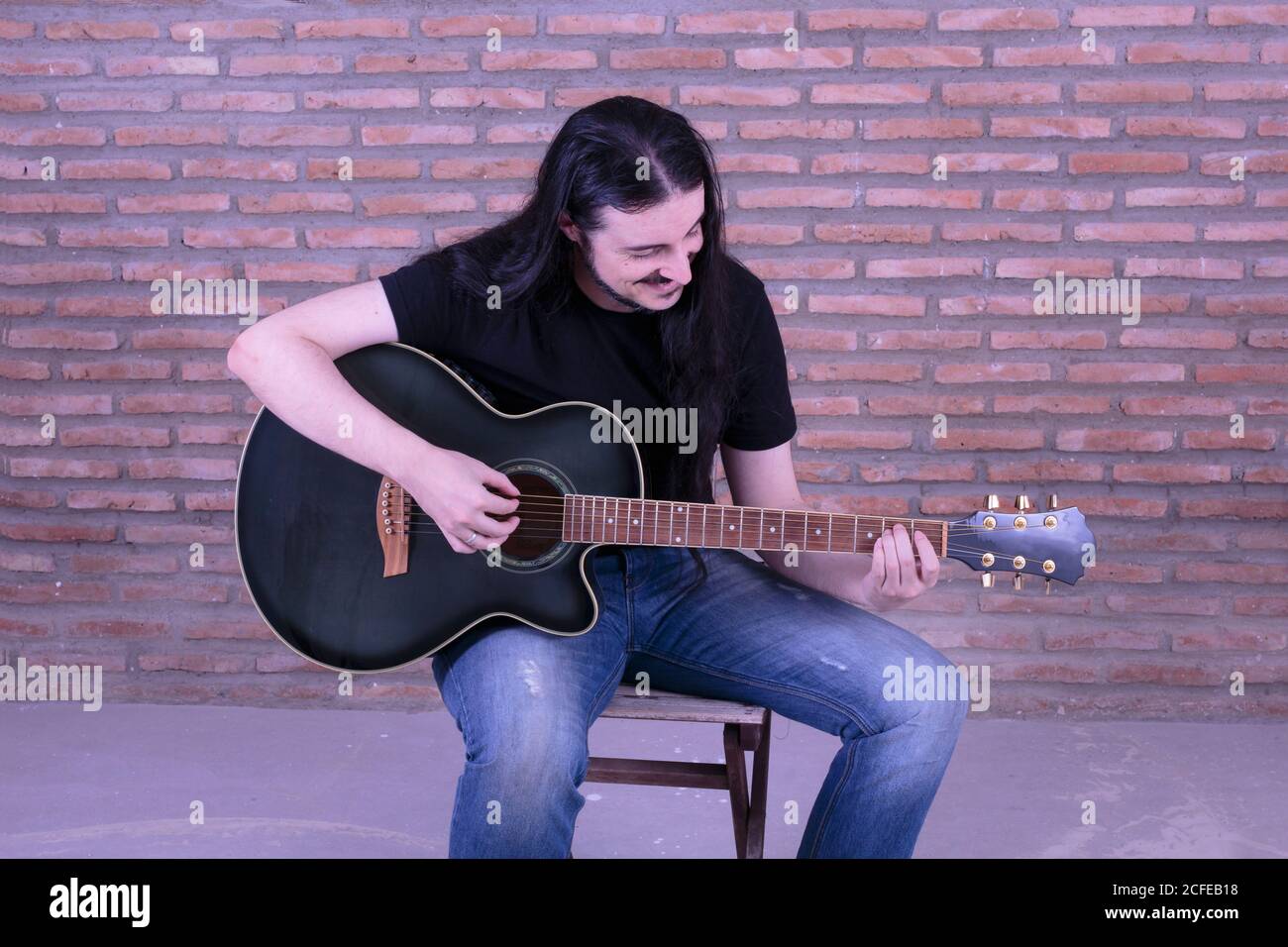 Young male performer playing guitar sitting on a chair. Stock Photo