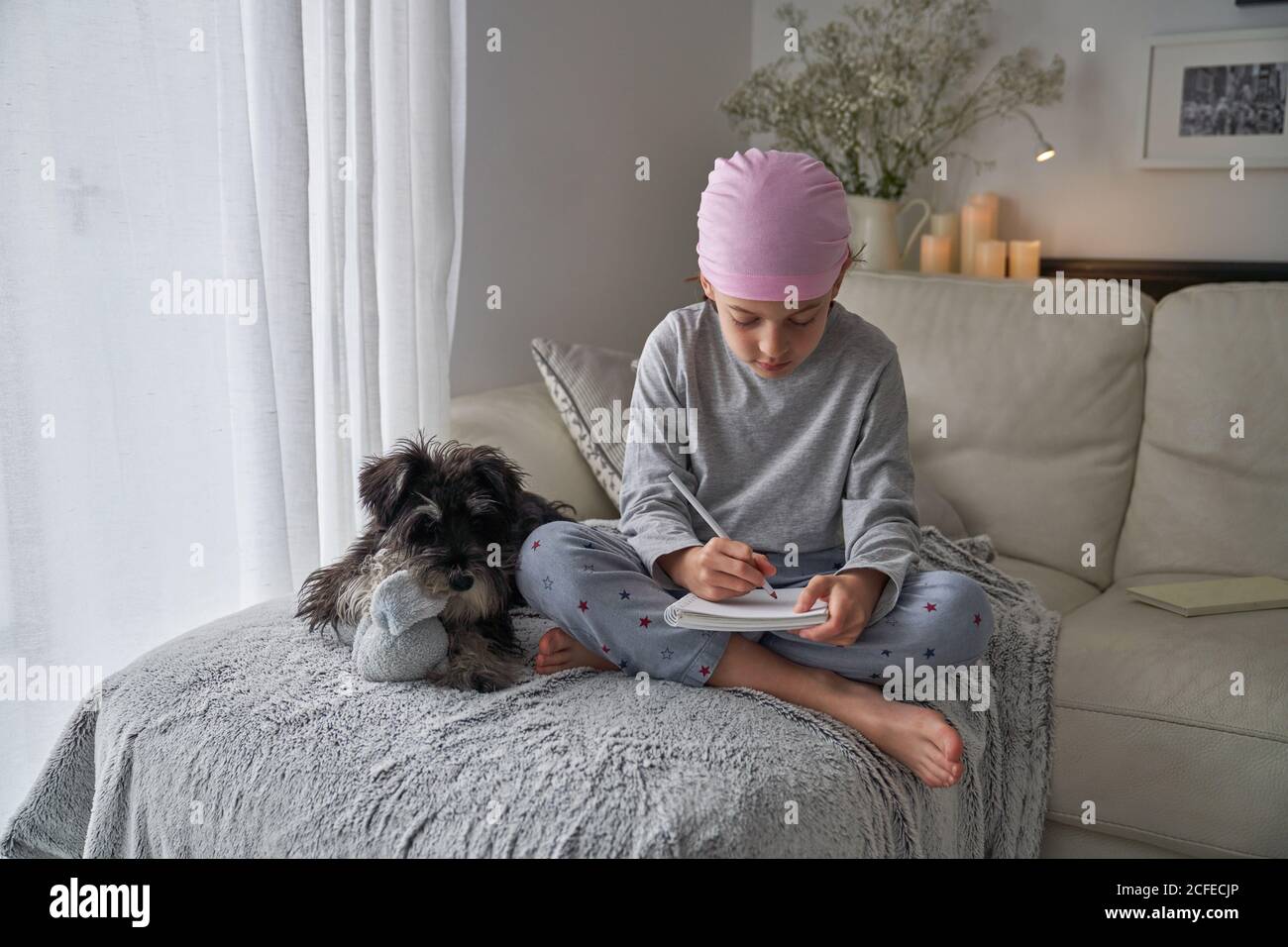 From below happy little child with cancer disease writing notes while sitting with dog on bed in room Stock Photo