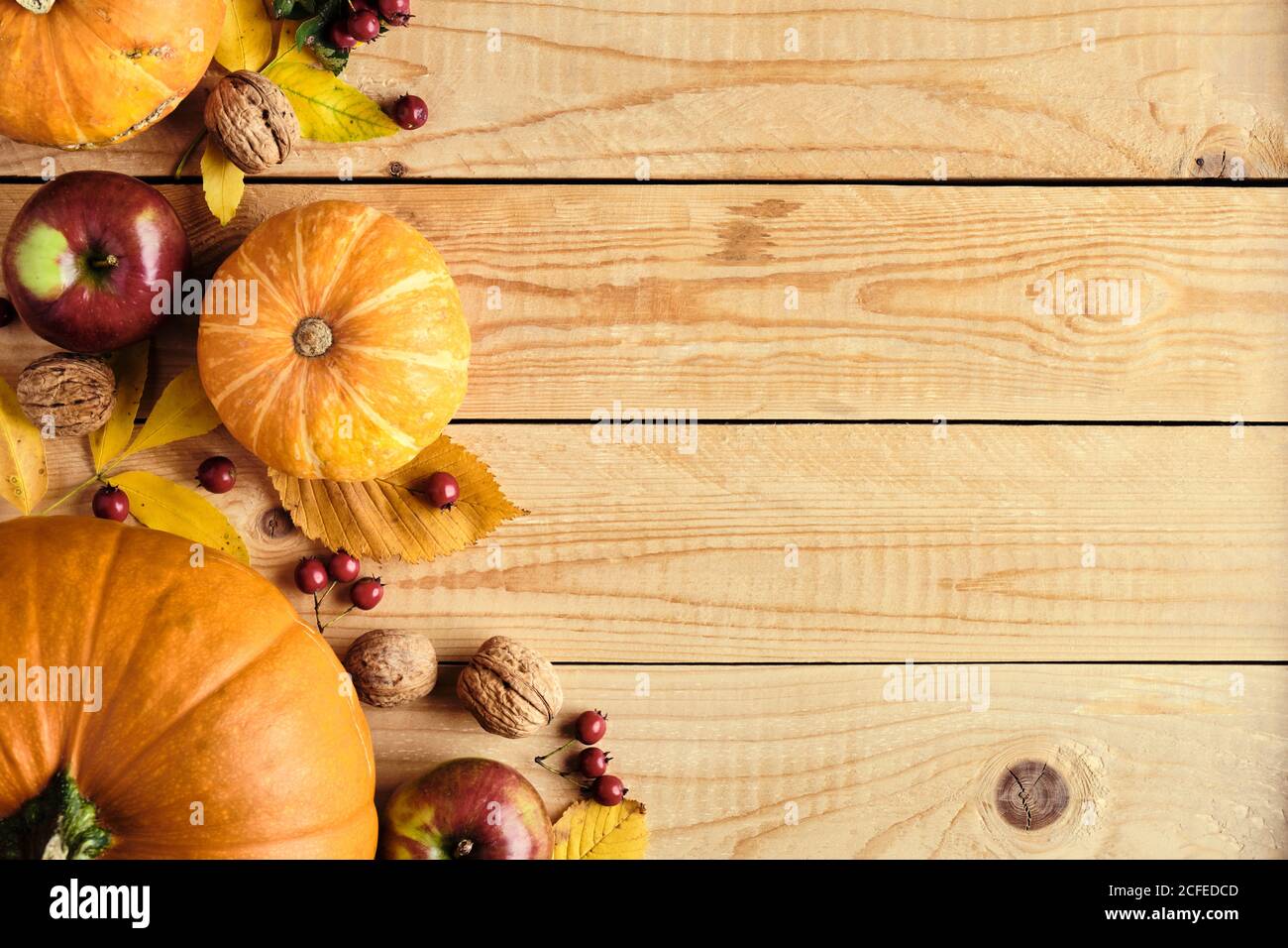 Autumn holiday concept with pumpkins, fallen leaves, nuts, red berries on wooden table. Thanksgiving background. Flat lay, top view, copy space. Stock Photo