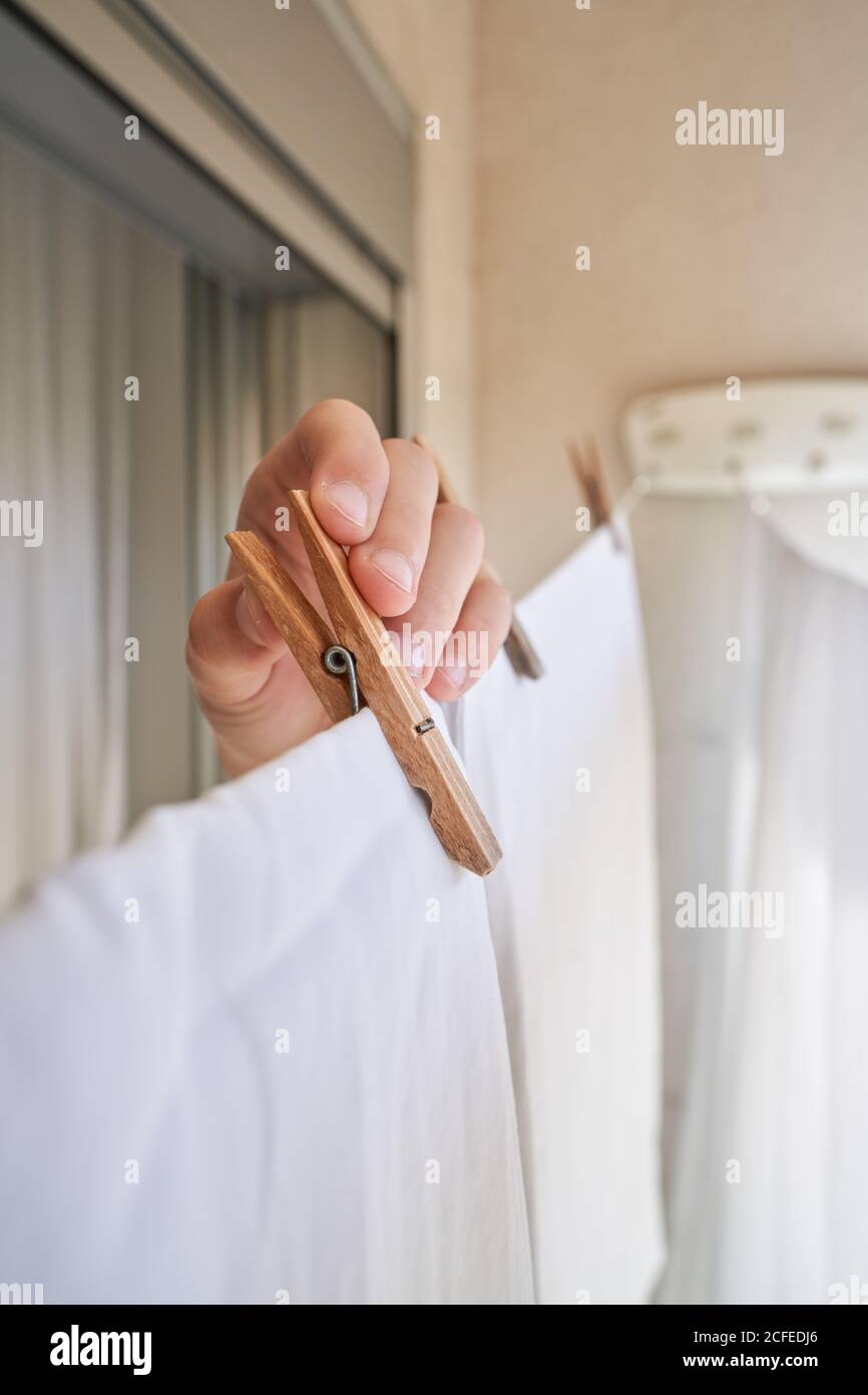 Cropped faceless person pinning wet white sheet on rope with clothespin while hanging linen to dry on balcony Stock Photo