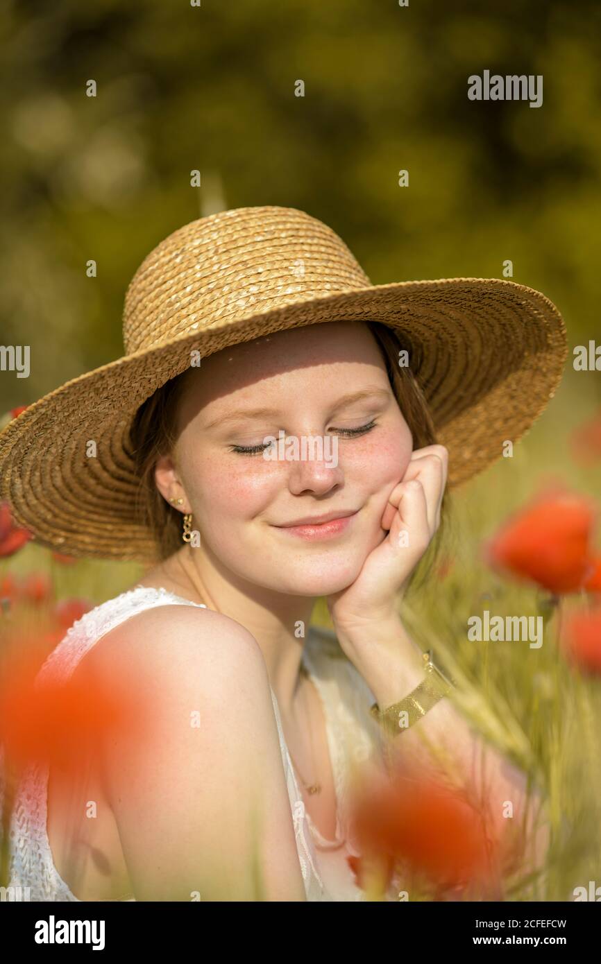 Young girl in a straw hat dreaming positive sitting in the poppy field Stock Photo